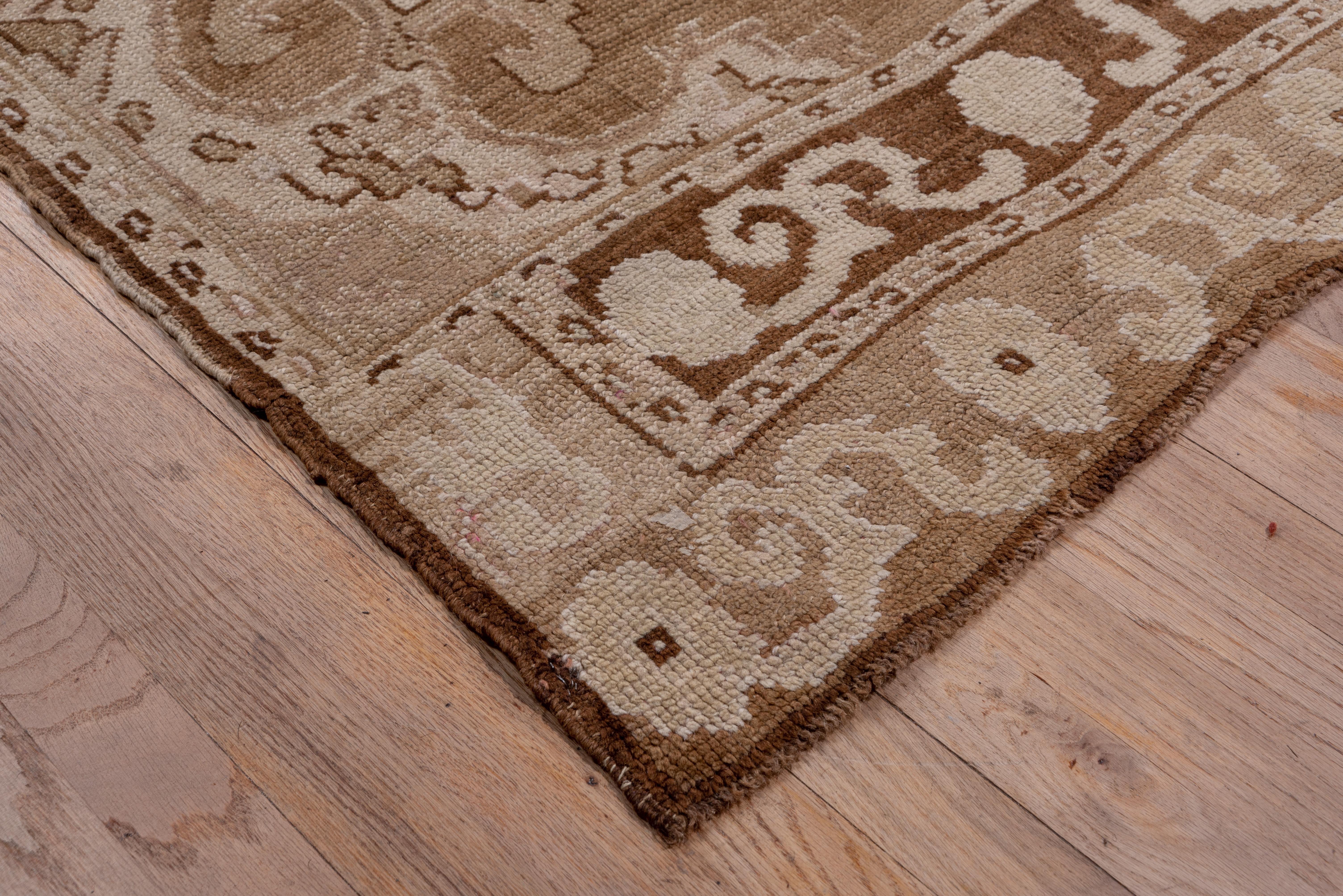 This coarsely knotted, western Turkish town carpet shows two columns, each of three pointed and rams horn hooked floating medallions, on a visibly abrashed open brown field. Double end borders with rosette and acanthus scrollery.