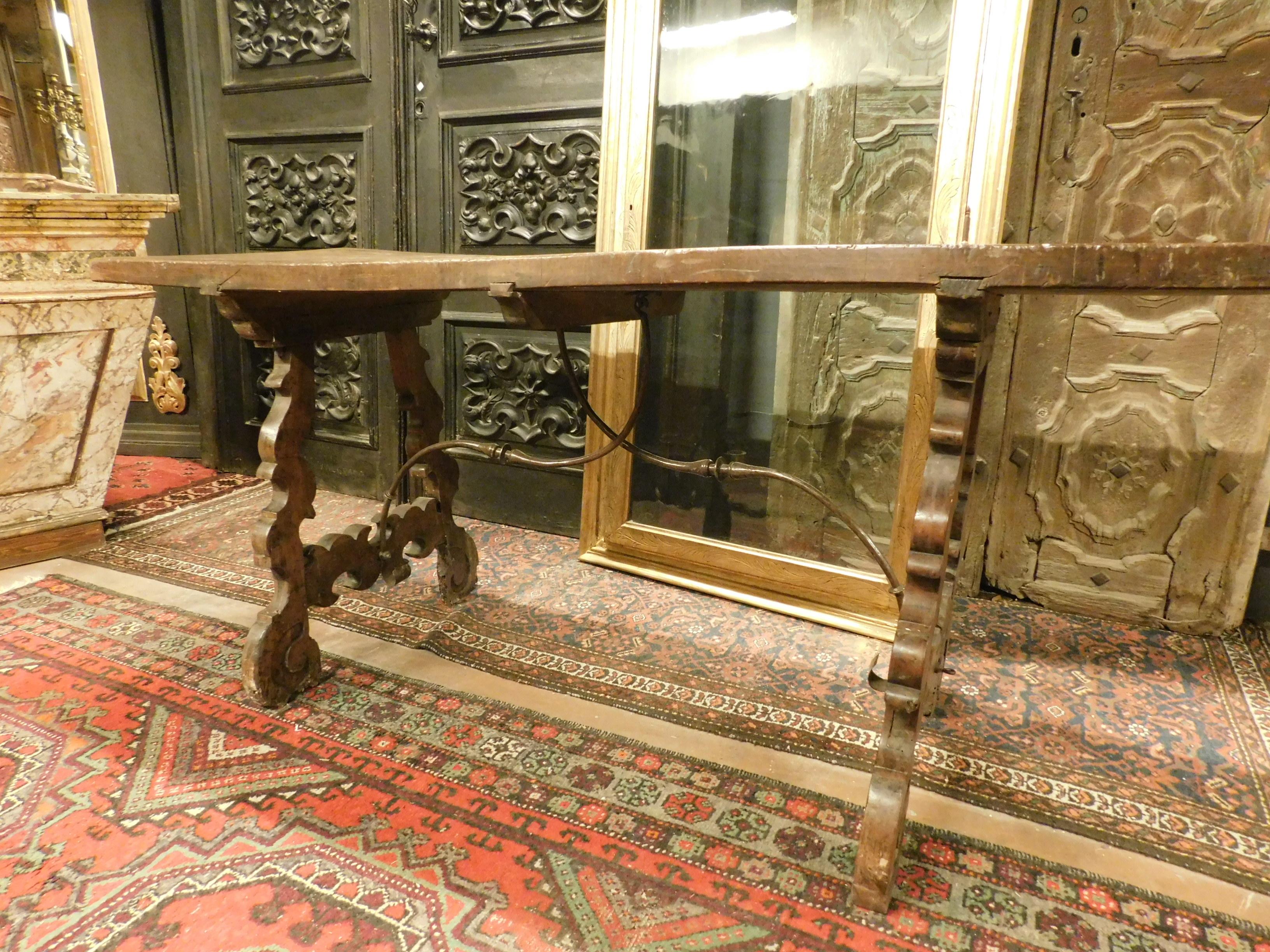 Antique dark brown walnut table, designed with a lyre style, formed by a single large plank, by now waved, the moved legs are typical of the 1700, it also has the original iron between the hand-sculpted wavy legs, coming from the house of nobles in