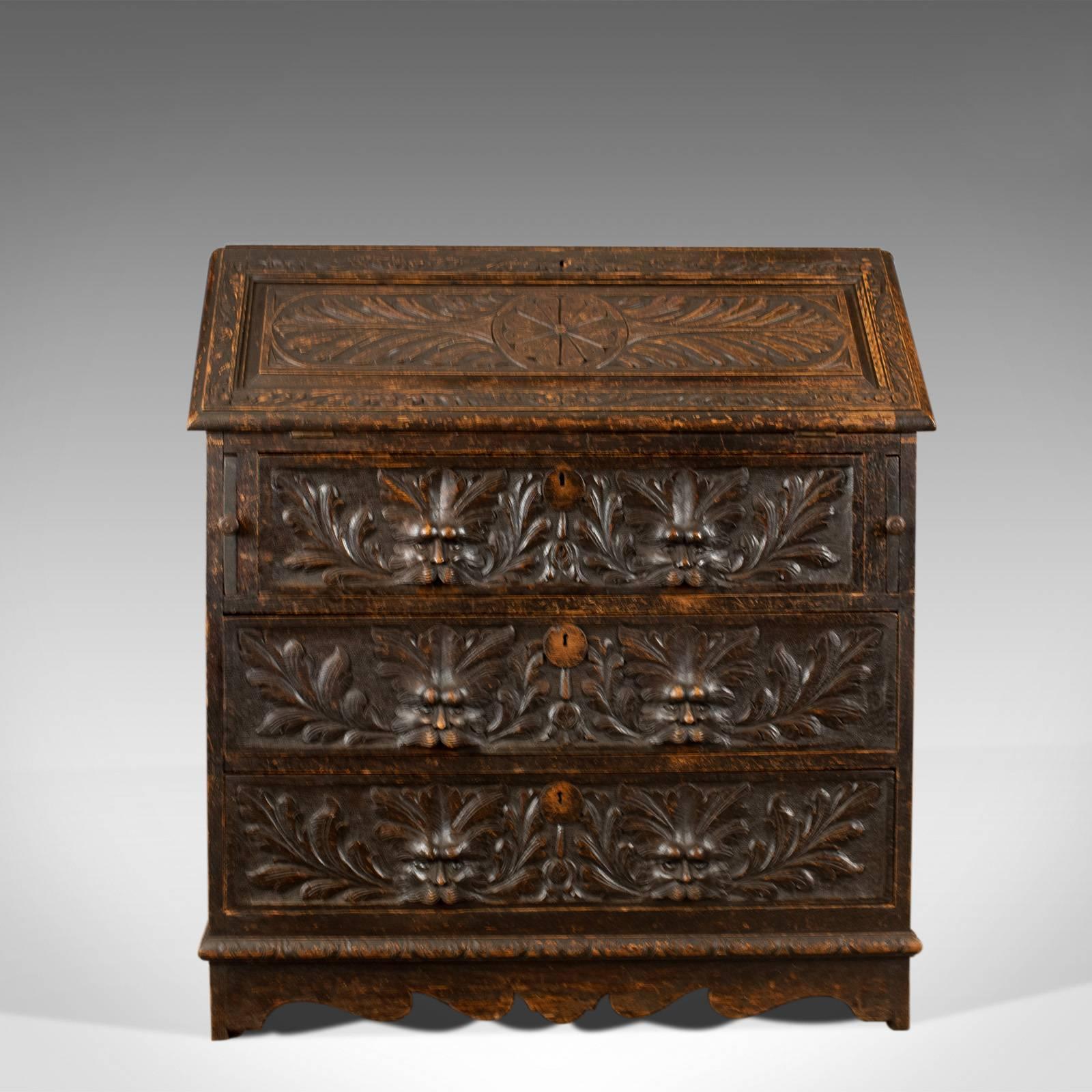 This is an antique bureau in English oak. A Victorian green man writing desk dating to circa 1880.

Warm country feel and a desirable aged patina in the wax polished finish
Profusely carved and decorated with green man masks and foliate