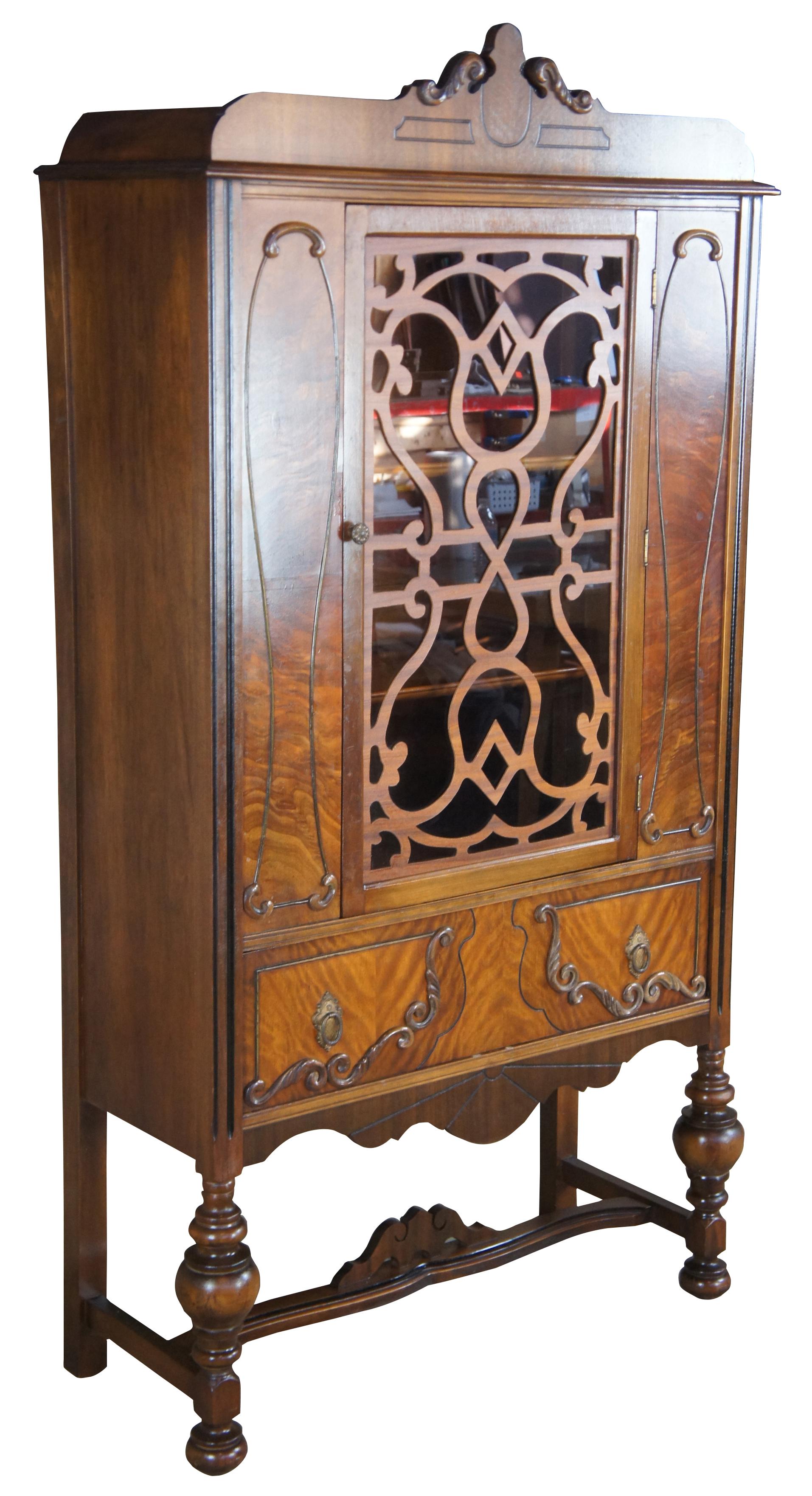 Early 20th century Jacobean style china cabinet. Made from walnut with a burled front. Features two shelves concealed by a large central door lined with fretwork over dovetailed silverware drawer. Includes a serpentine crown and lower apron. The