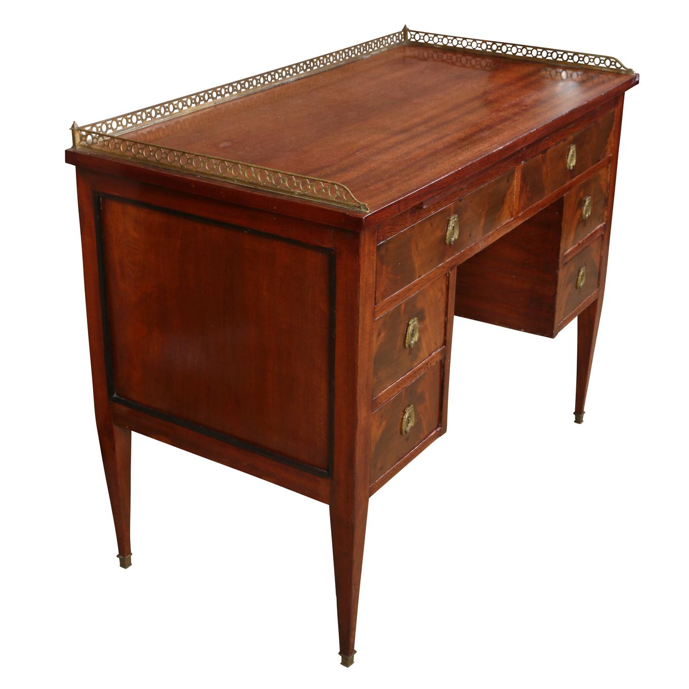 A petite burled wood antique desk with brass gallery rail and brass decorated hardware surrounding each drawer's keyhole. Beautiful burled wood on the face of each of six drawer faces and the desk top has beautiful wood grain running through it and