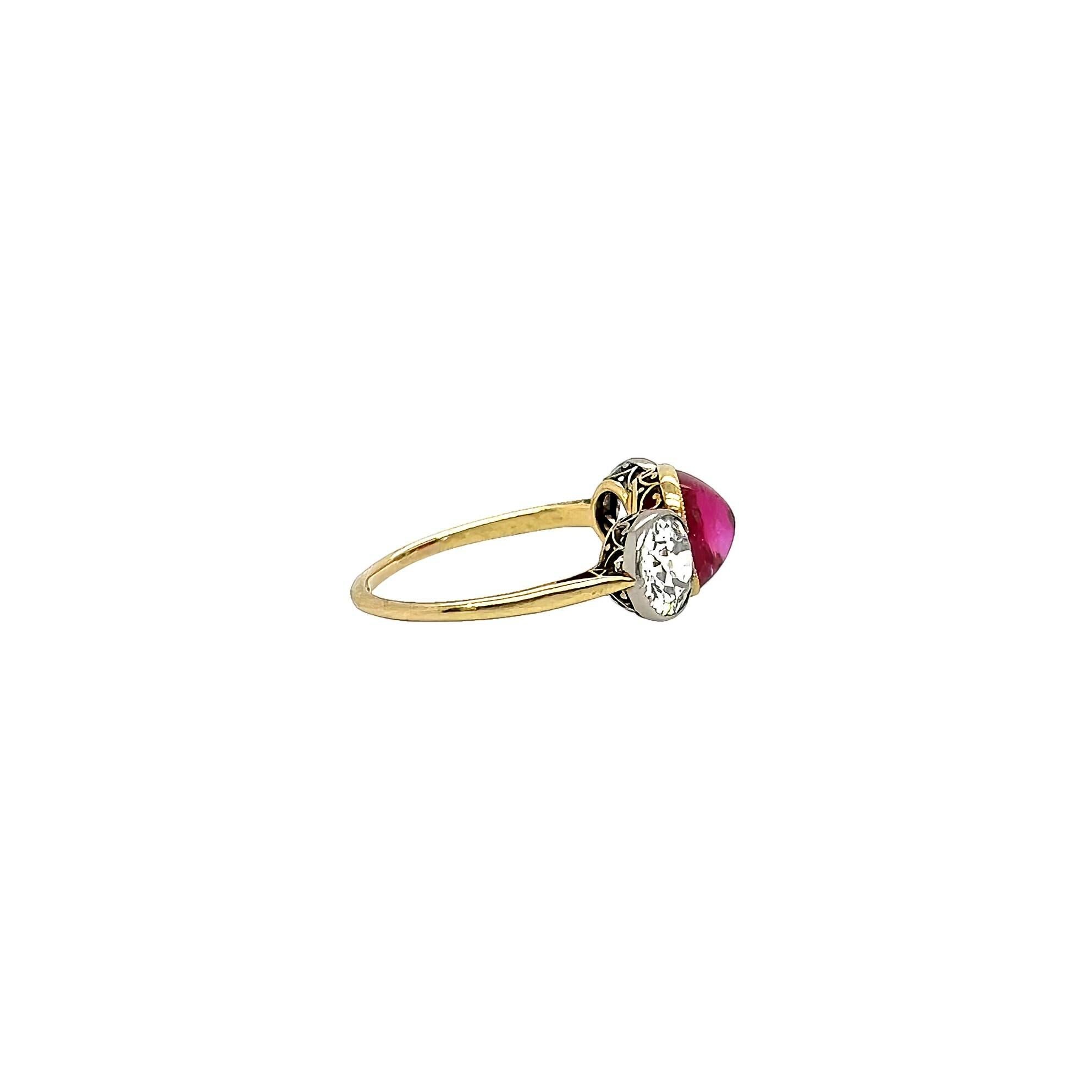 A yellow gold, platinum, ruby and diamond ring, circa 1905.  Centering a gold bezel set oval cabochon unheated Burma ruby weighing approximately 3.08 carats* flanked by two platinum bezel set old European cut diamonds weighing approximately 0.87 and