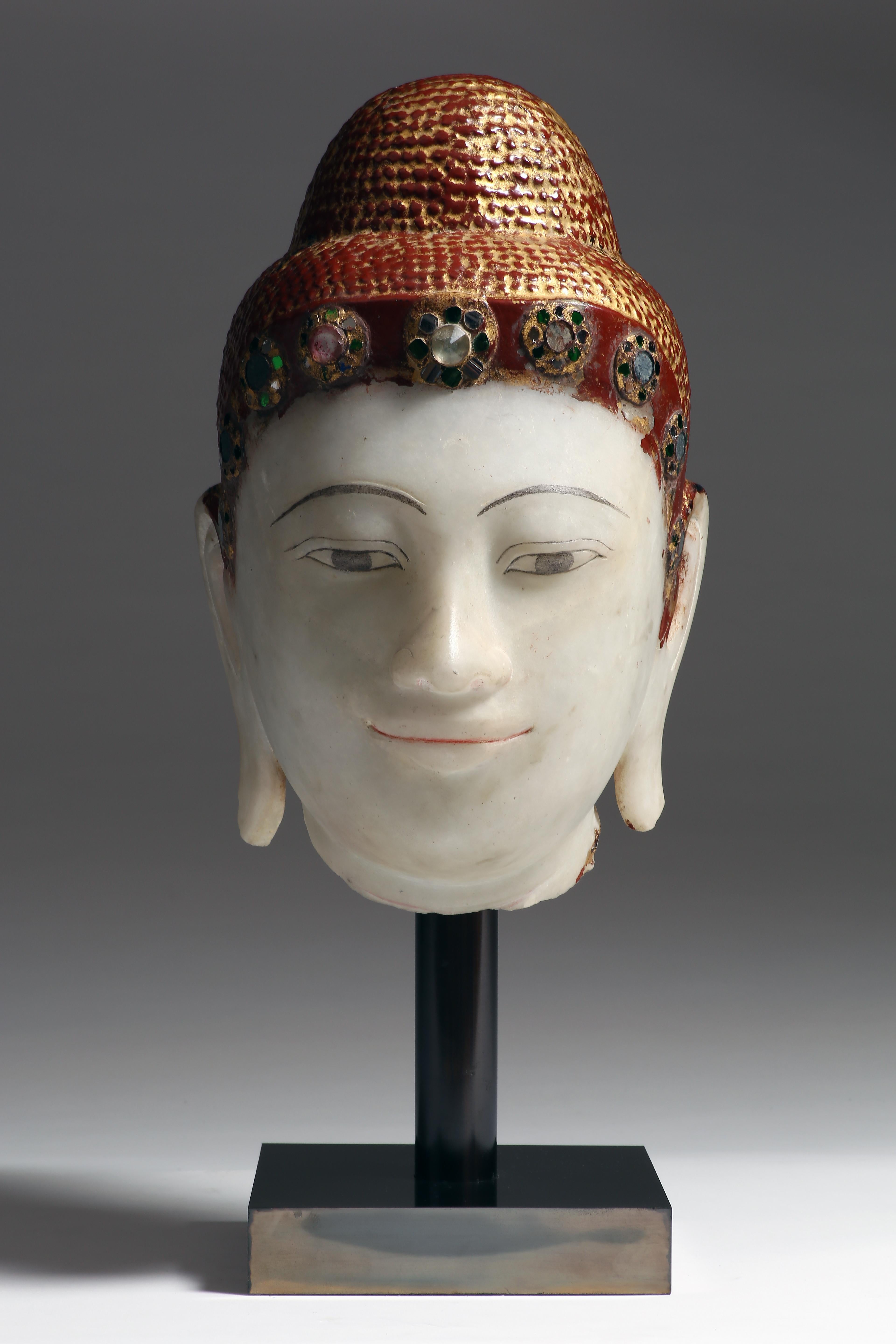 The face is carved with a meditative expression, slit eyes set under arched eyebrows, aquiline nose and smiling lips, elongated earlobes, curled hairdress and usnisha. Glass (hman-zi shwei-cha) decoration is inlaid on the hairdress band. Gilt and