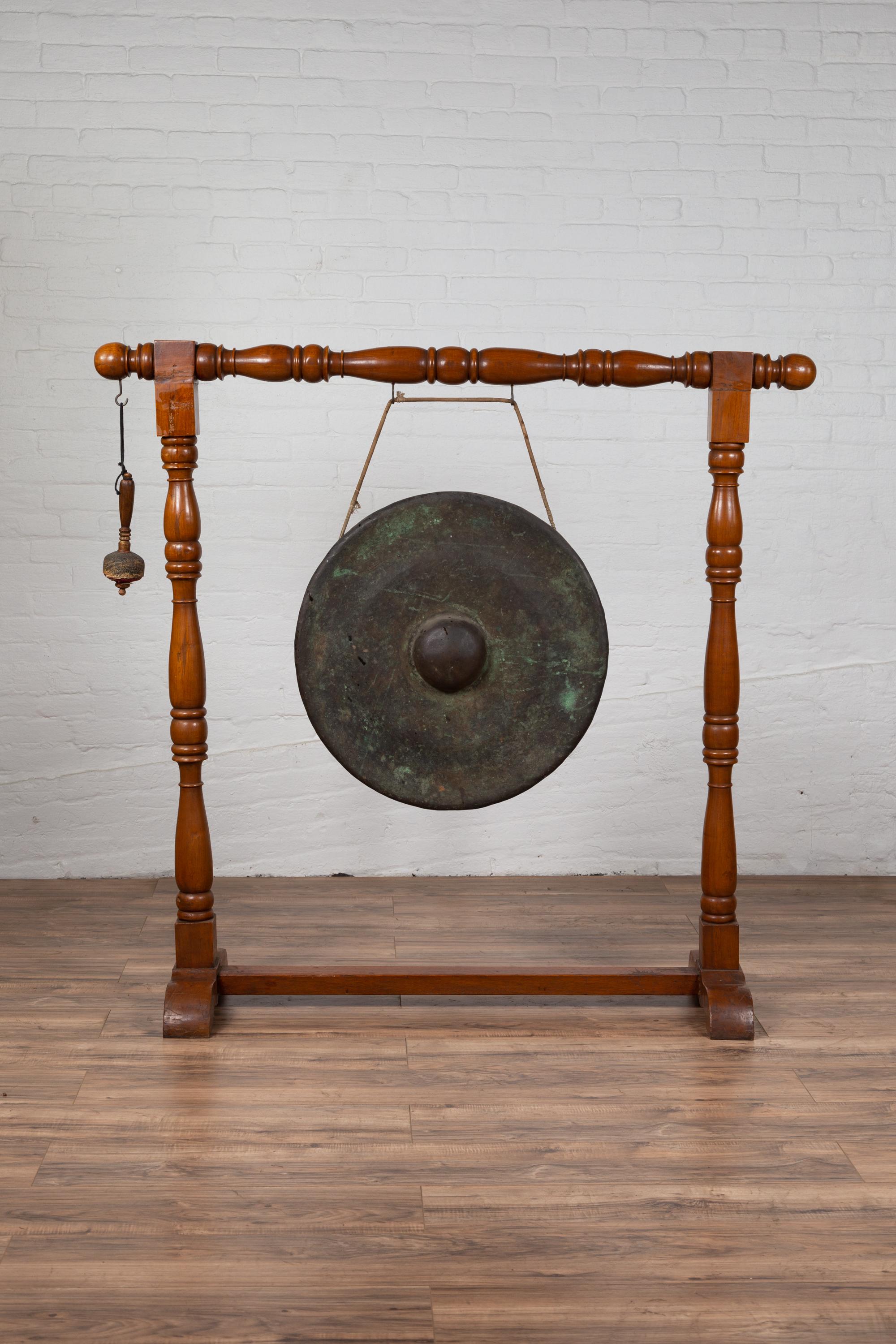 An antique Burmese bronze temple gong with mallet from the early 20th century, mounted on a wooden stand. Born in Burma during the early years of the 20th century, this exquisite bronze temple gong features a traditional circular shape accented with