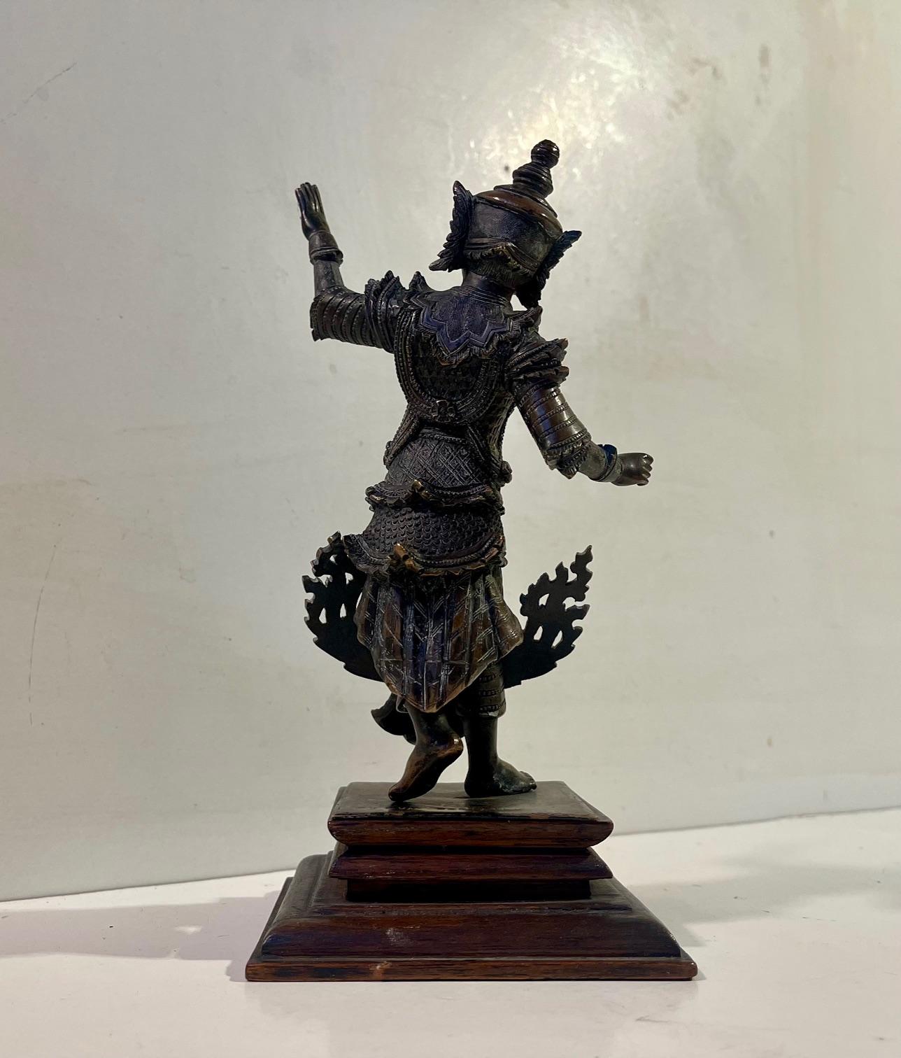 An exceptionally well-cast figure of an elegant male Burmese court dancer in traditional dress. The figure is mounted on its original wooden stand. It stands balanced on one foot and with both arms in elegant motion. The base is stamped Mandalay and