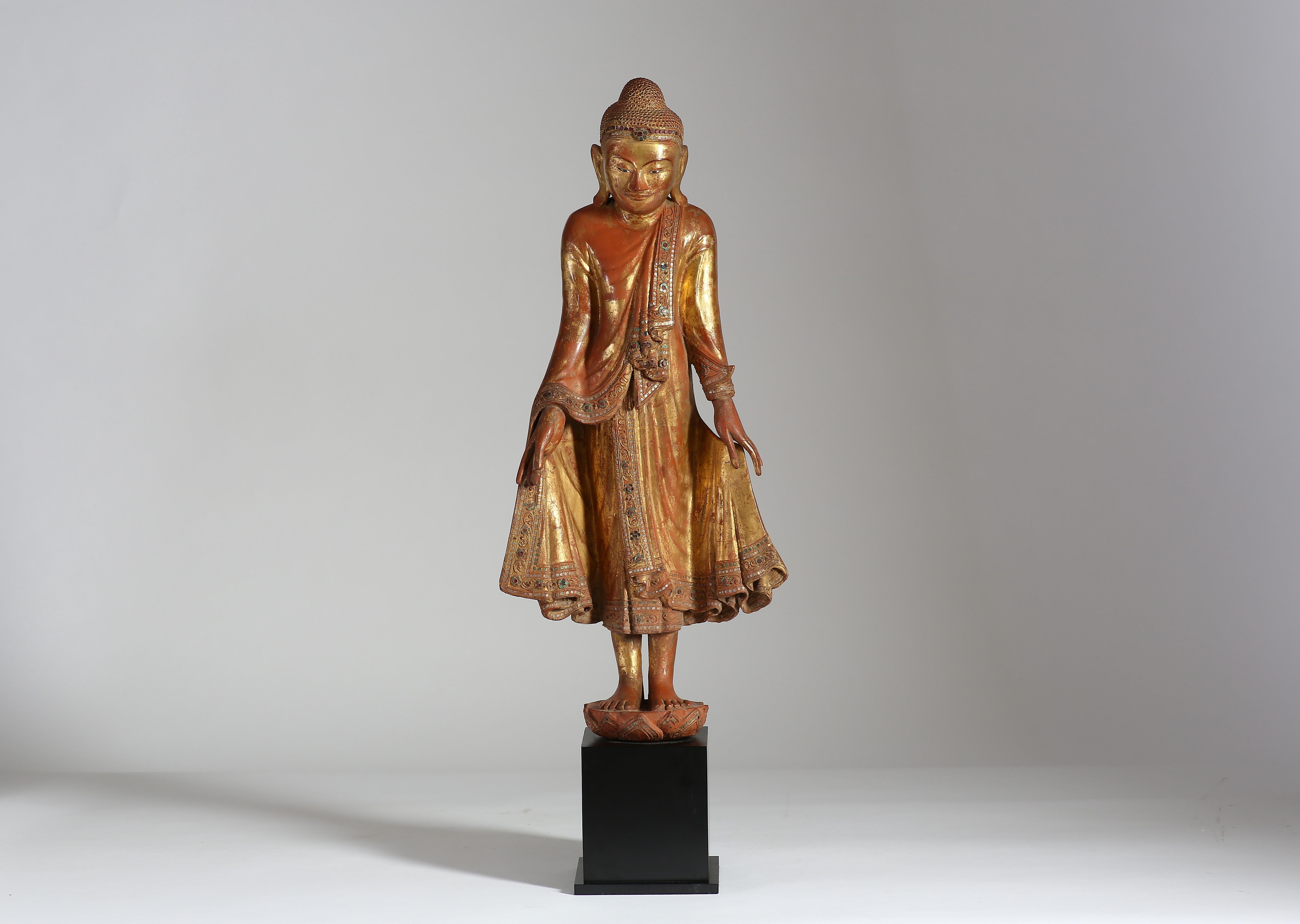 In piedi su un piedistallo di loto, con entrambe le mani che stringono la veste, finemente scolpita con flussi e fronzoli della veste e decorata con vetri colorati, il Buddha ha un'espressione serena, gli occhi abbassati sotto le sopracciglia