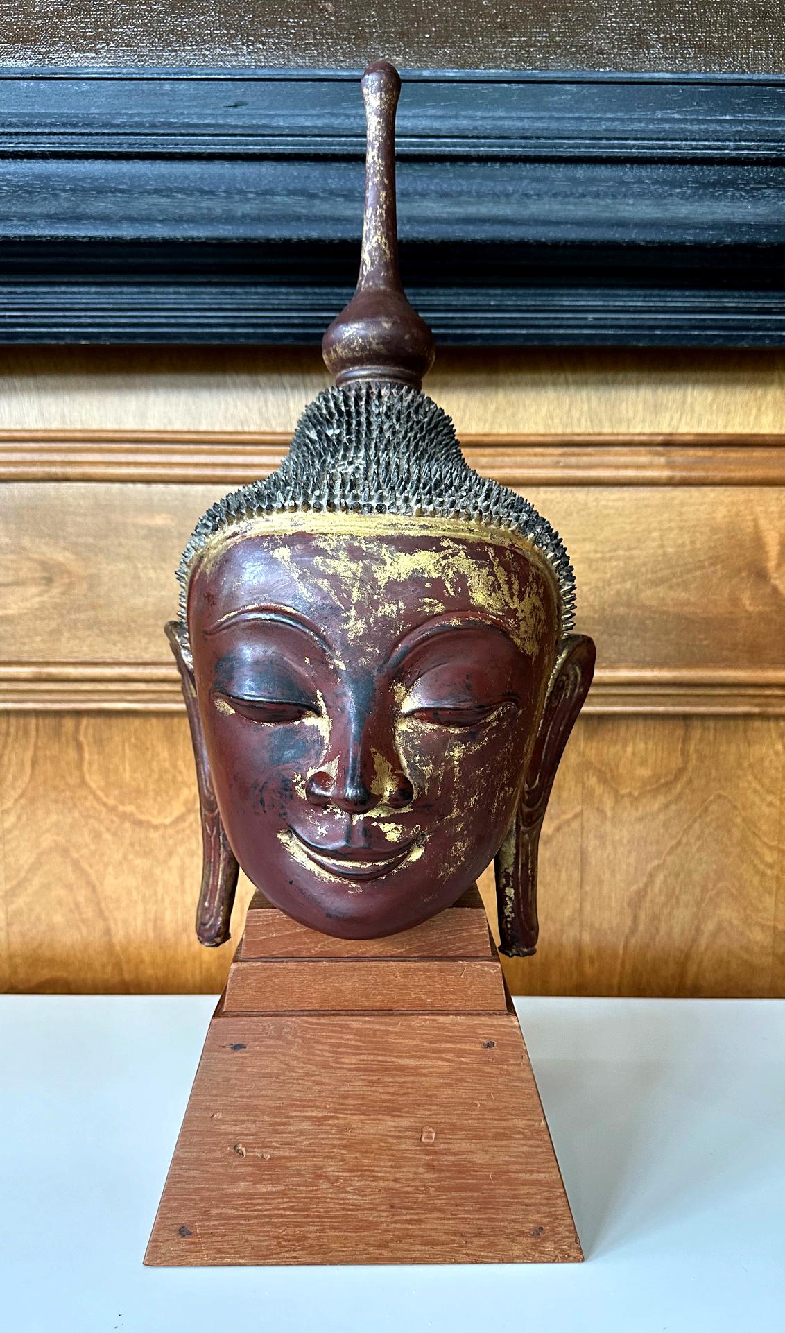 An antique lacquered and gilt wood buddha head on a custom wood stand circa early 19th century. The statue was finely sculpted with a wood core and the surface was decorated with a dark red lacquer with remanent of gold leaf gilt. This type of