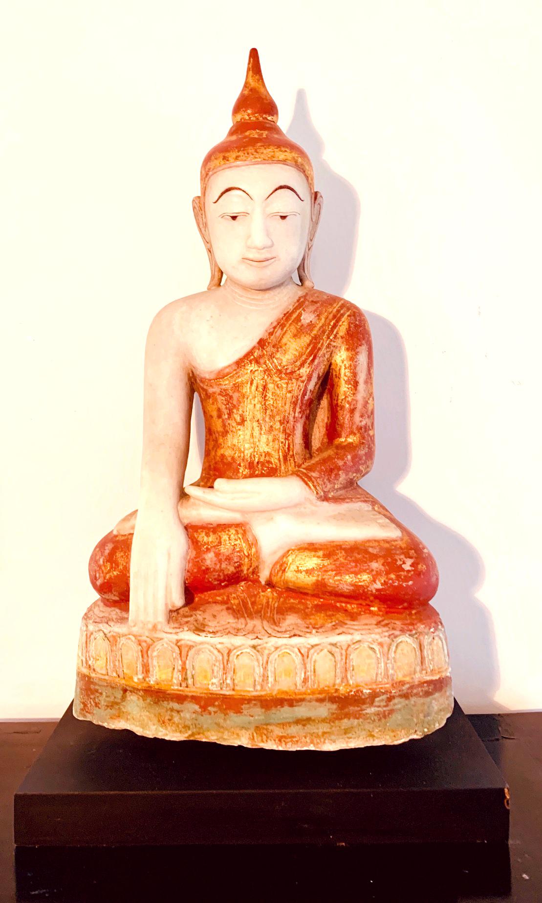 Finely carved from a solid block of white marble and decorated with red and gold pigments, this Buddha statue is depicted as seating on a lotus throne in an 