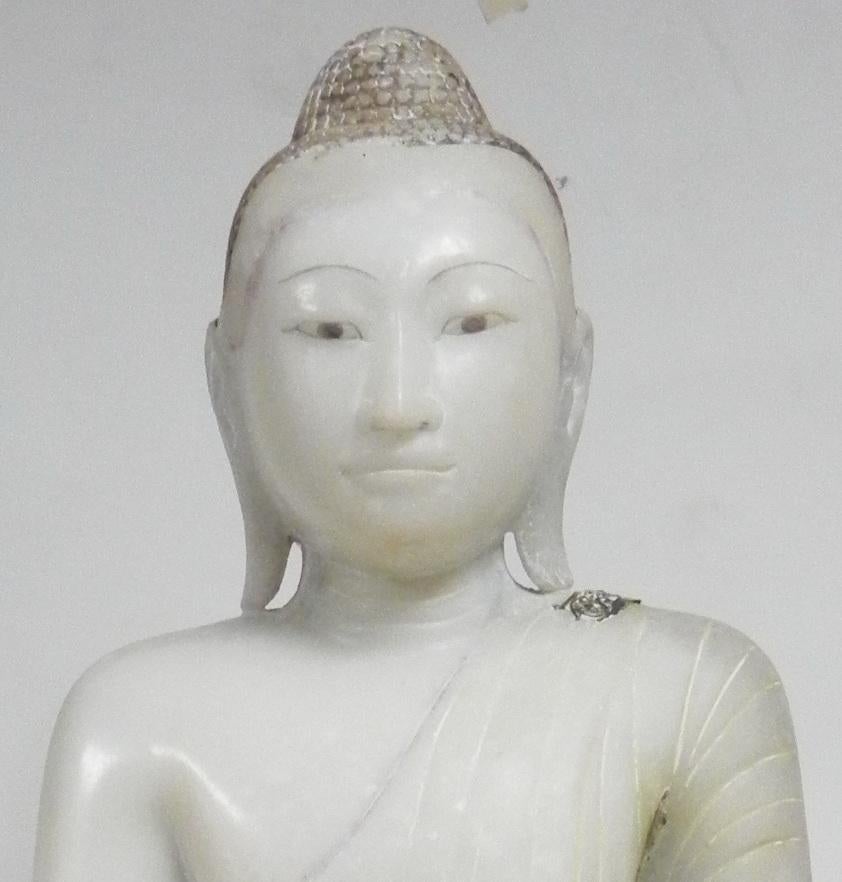 The Buddha seated in virasana on a shaped base, his right hand in bhumisparsa mudra – calling the earth to witness, the left in dhyana mudra – meditation, wearing samghati finely carved with folds of flowing fabric, leaving the right shoulder