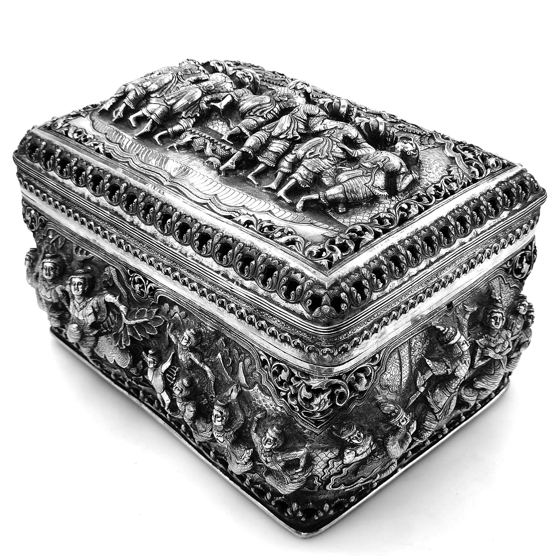 A magnificent Antique Burmese solid Silver Box with a rounded rectangular form. The sides of the Box and the lid are embellished with chased ornate designs in deep relief. The chased designs on the Box show groups of figures surrounded by trees. The