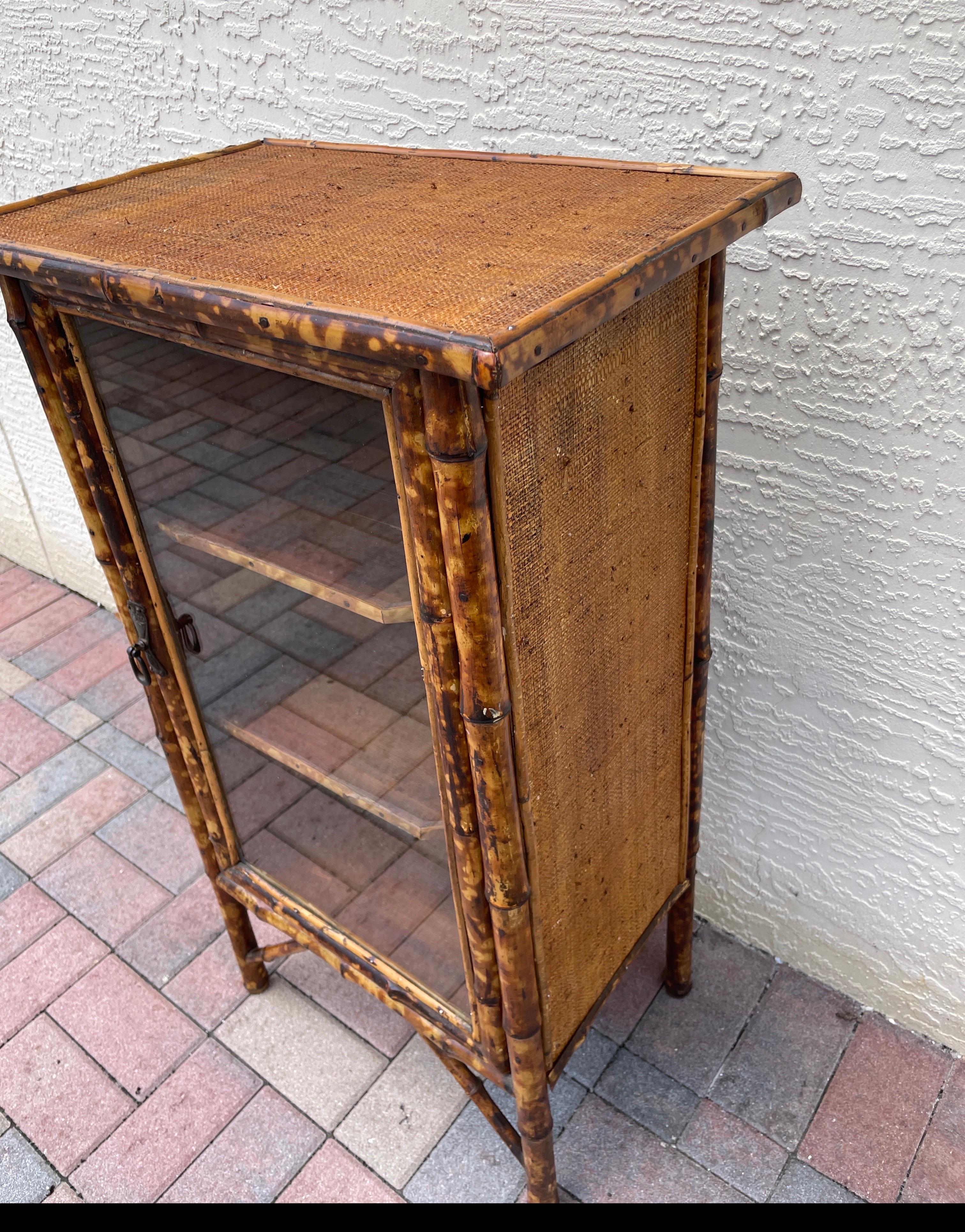 Antique burnt bamboo cabinet with single glass door and three interior shelves. Sides and top covered in raffia.