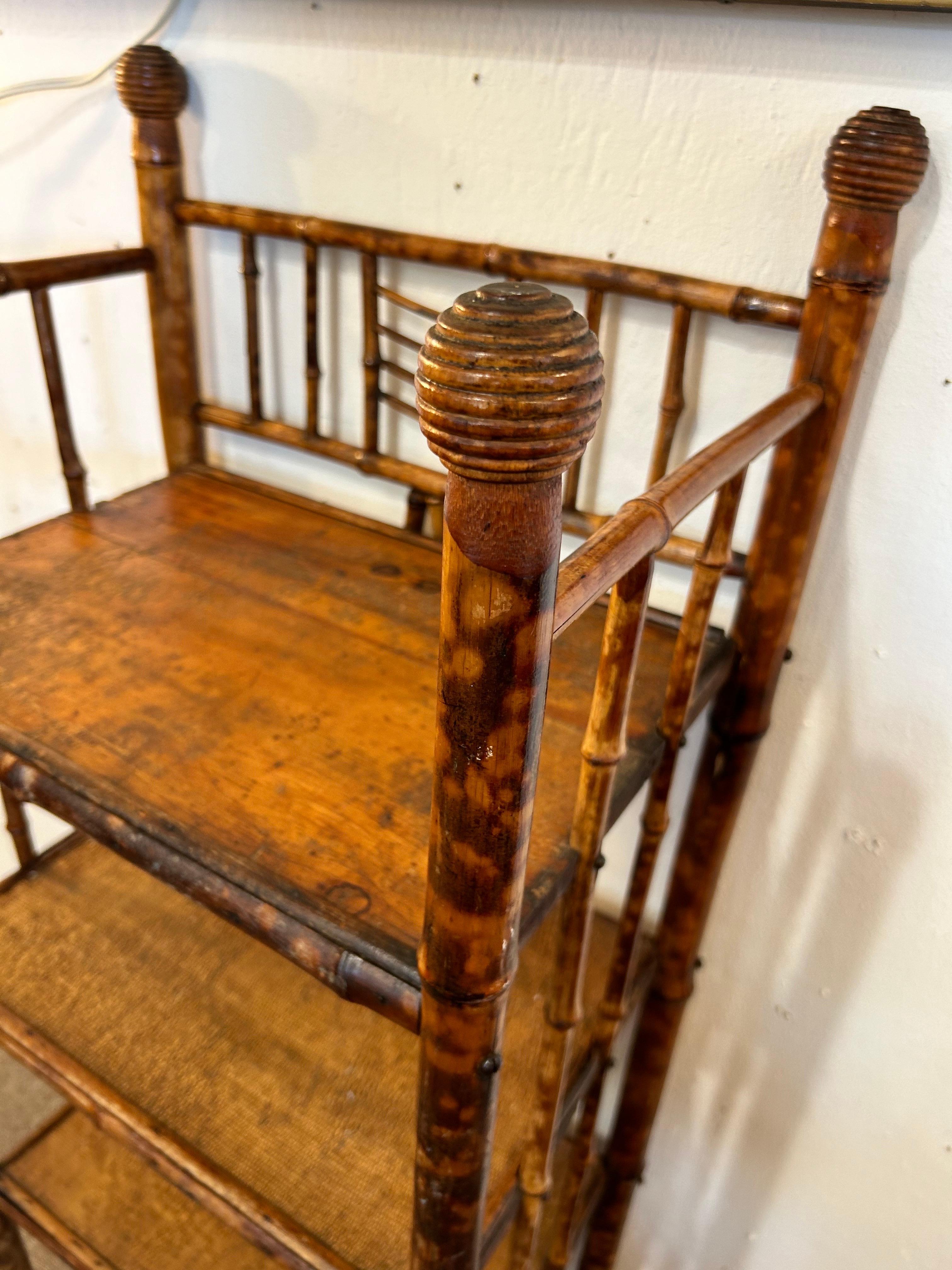An antique circa late 19th century burnt bamboo four shelf etagere. The tops of the four corner supports each result in a grooved, egg shaped knob as decoration. The back and sides of the shelving unit feature additional pieces of bamboo arranged in