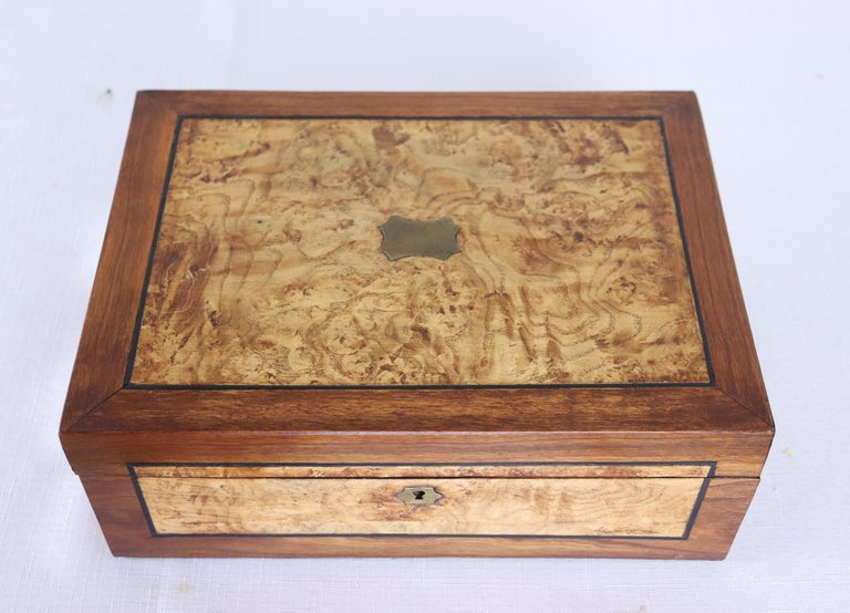 An oak jewelry box with fine burl elm inlayed panels and ebony stringing all around. Brass accent on top and around the keyhole. The interior retains its original paper. No key.