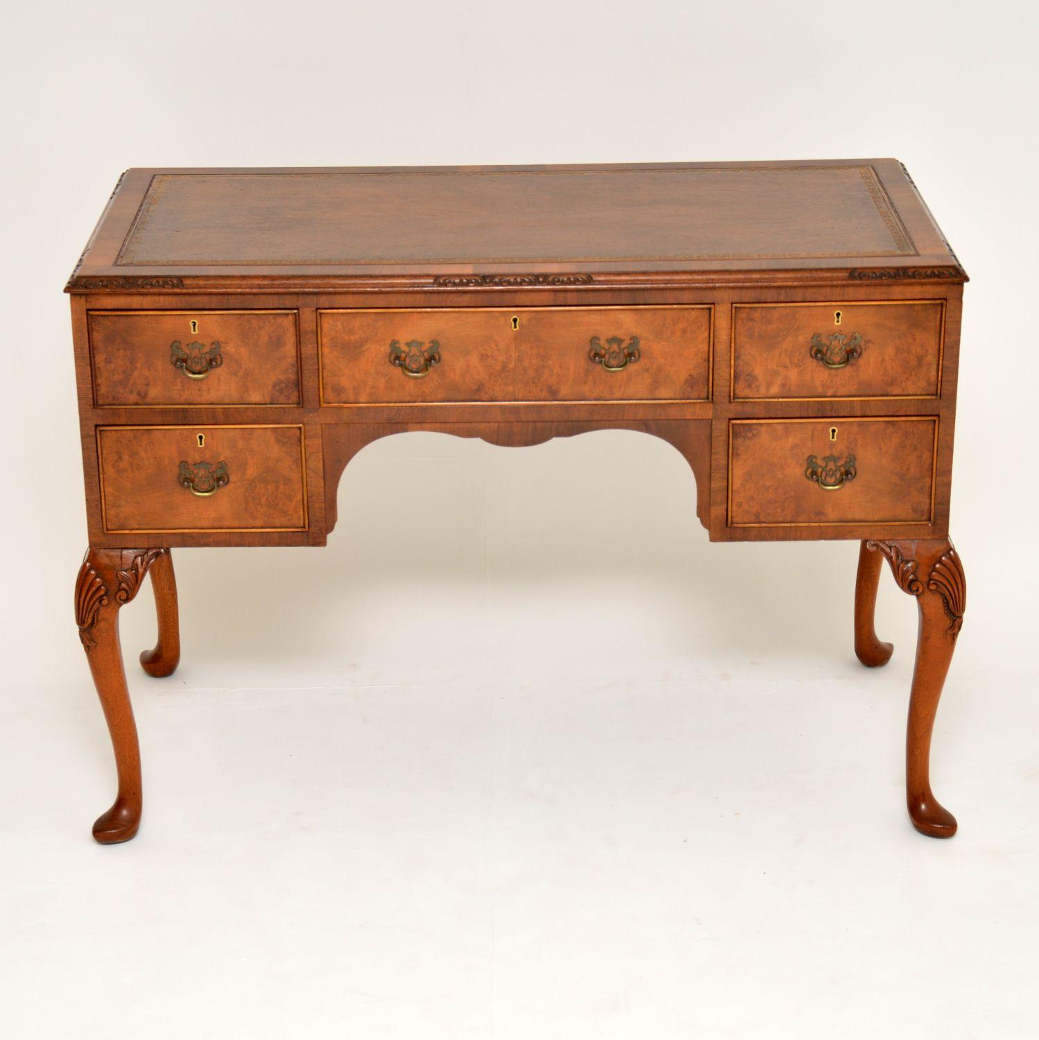 Fine quality antique Queen Anne style walnut leather top desk is excellent condition & dating from circa 1930s period. It has a tooled leather writing surface & a top edge that’s intermittently carved all the way around. The drawer fronts are burr