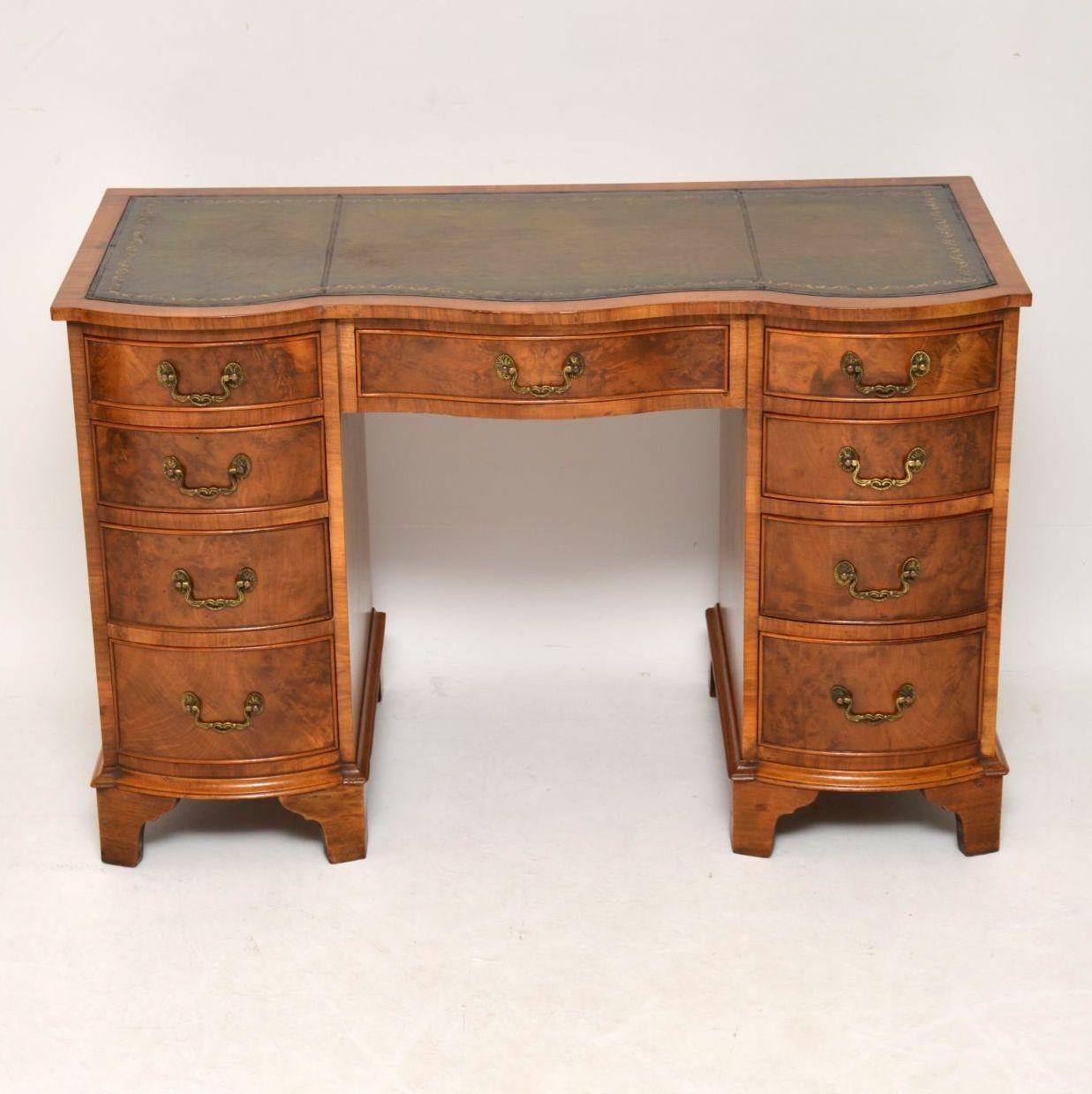 This antique Georgian style burr walnut desk is not too large, but still has a generous kneehole space. It has a double serpentine shaped front and a tooled leather hand colored leather writing surface. The pedestal drawers are all graduated in