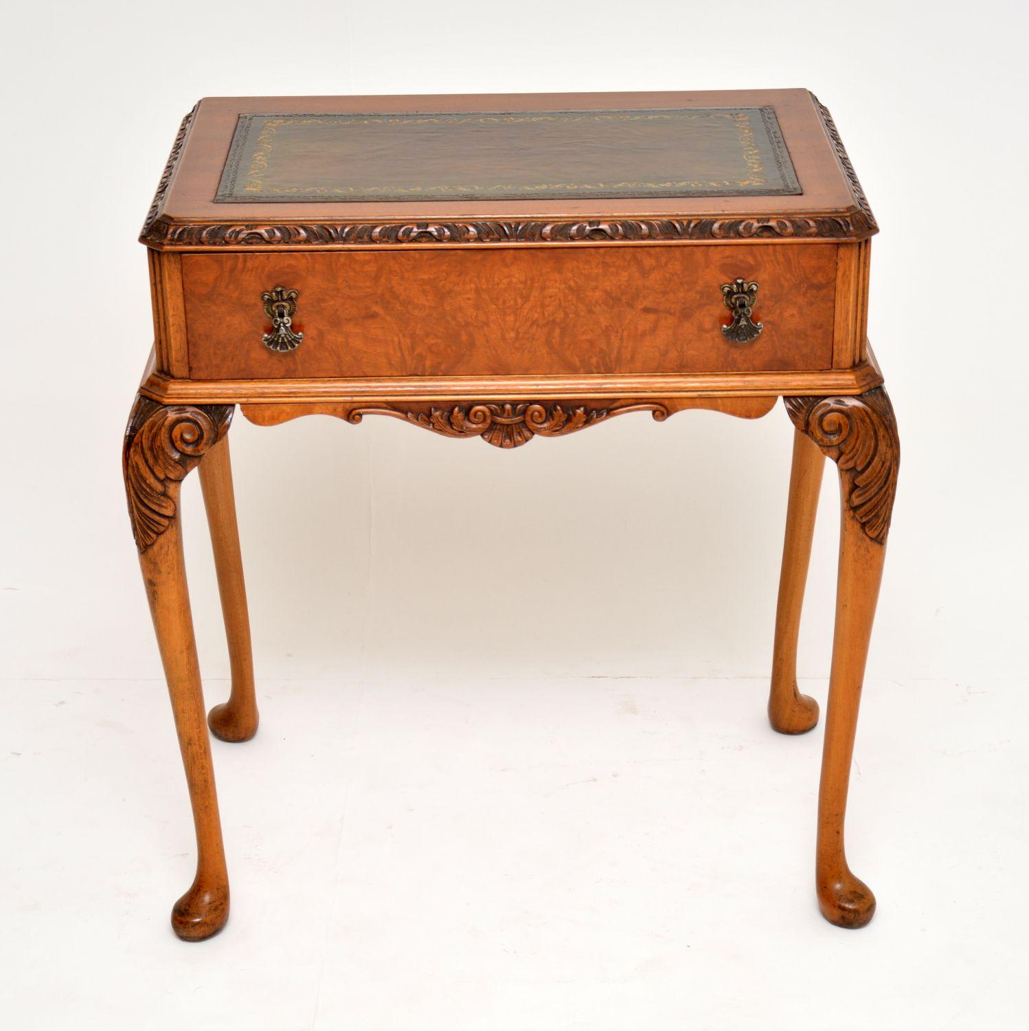 Small antique Queen Anne style walnut writing table desk with a tooled leather writing surface. It has grooved canted corners, a carved top edge, plus carvings on and between the solid walnut legs. The single drawer has a burr walnut front and