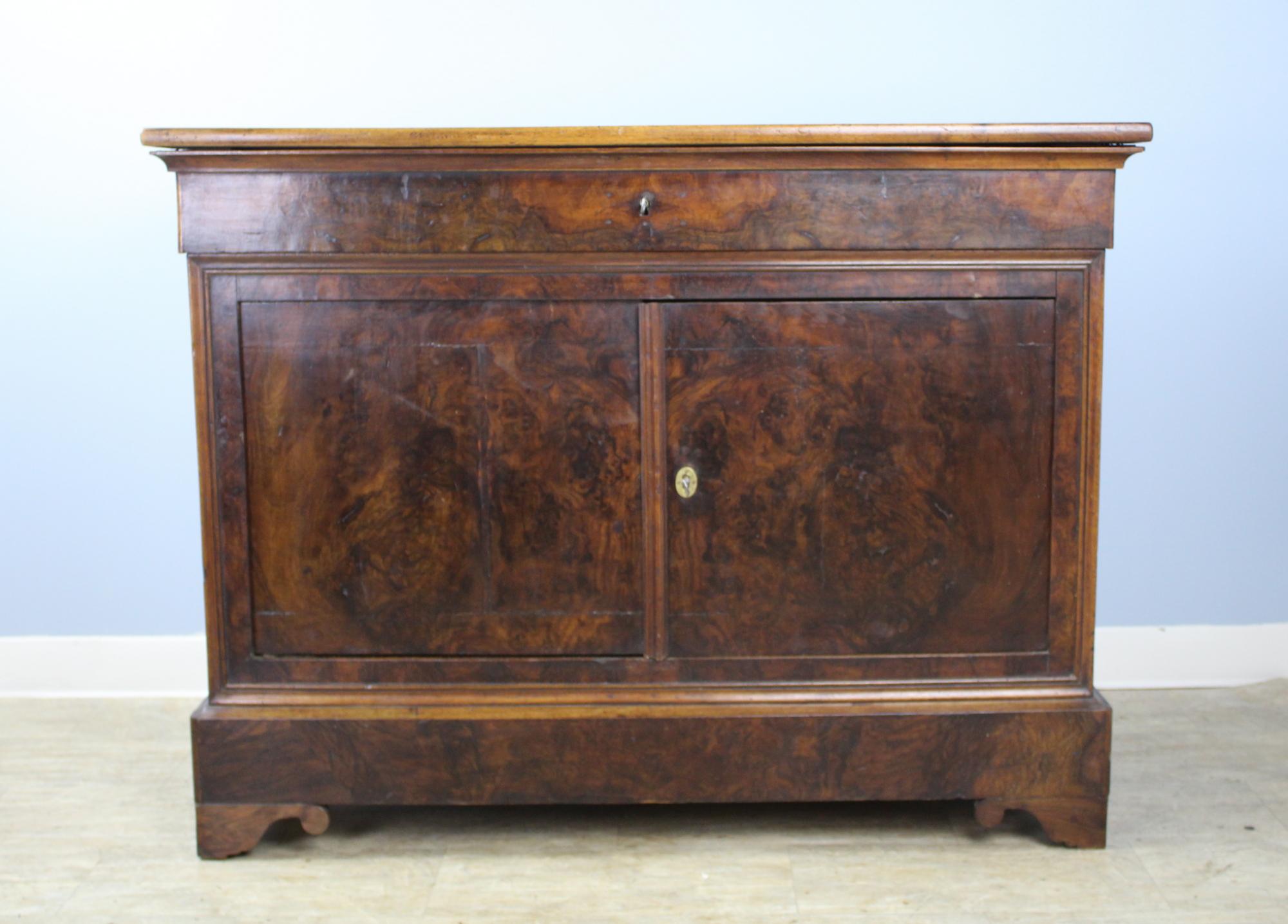 A handsome Louis Philippe buffet with a solid walnut top and burr walnut veneered front and sides. Elegant articulated feet under dramatically grained doors. The doors lock with original key and shut snugly with a simple spring latch. There are some