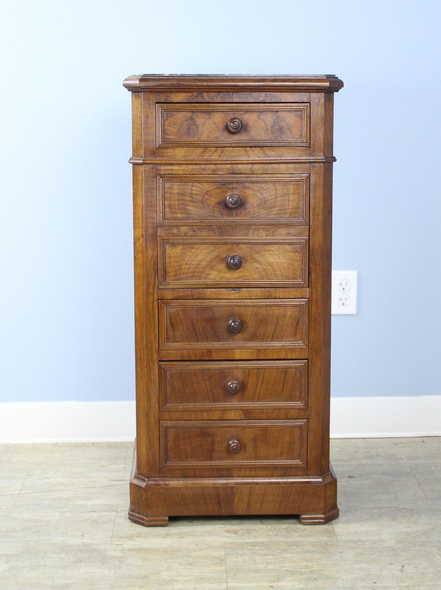 A handsome small cabinet or nightstand in mid walnut with its original light gray marble top. Although this piece appears to have six drawers, the second two are actually the door to a drop down cupboard which provides nice storage. There are four