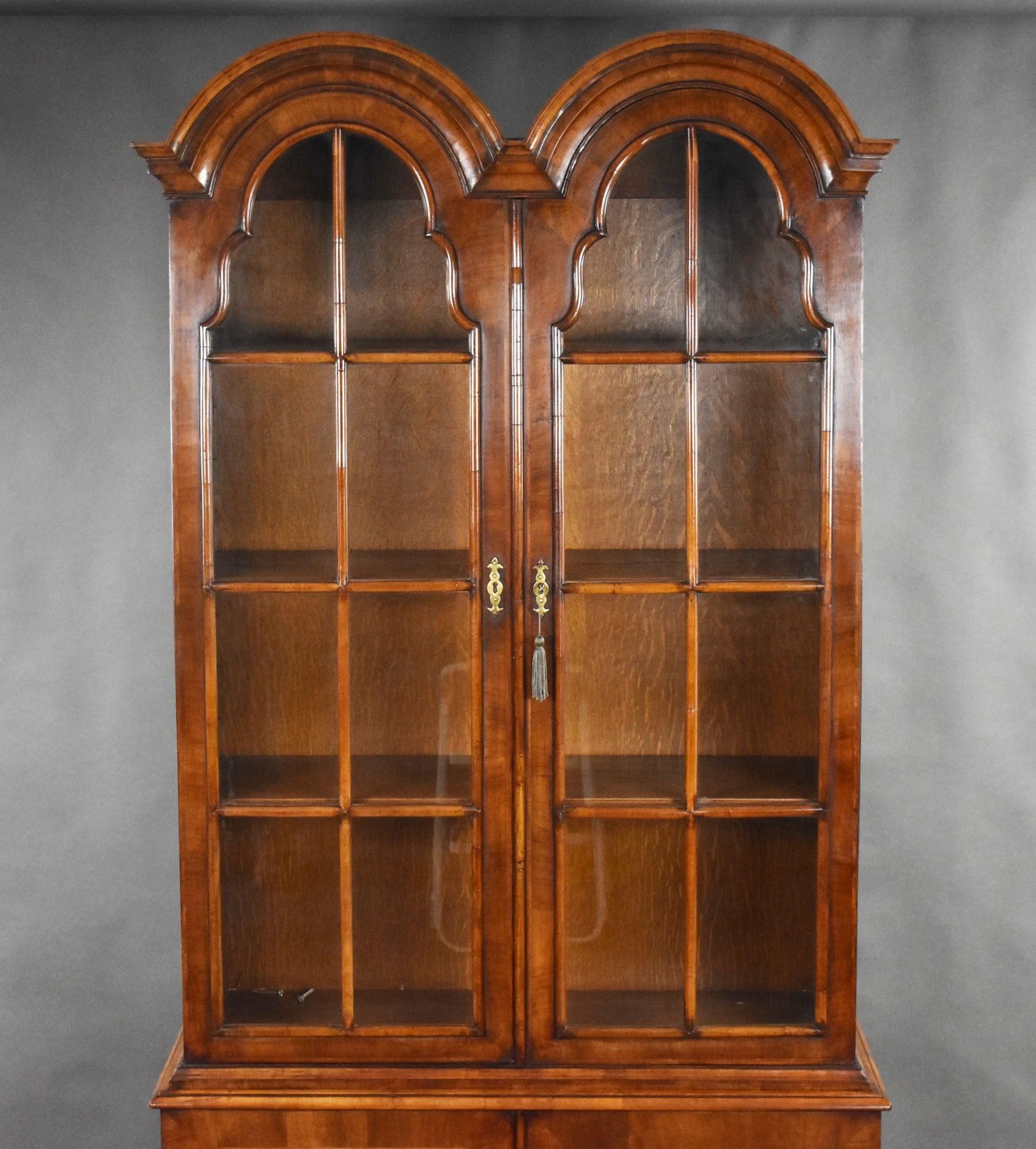 For sale is a good quality Queen Anne style antique burr walnut bookcase, having a double dome top with cross grain mouldings, above two glazed doors opening to two shelves, above a base with cross banded doors and herringbone inlay, raised on ogee