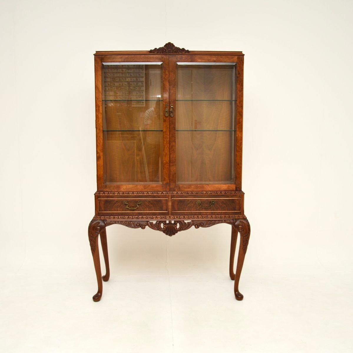 Superbe vitrine ancienne en ronce de noyer de style Queen Anne. Il a été fabriqué en Angleterre, il date des années 30 environ.

La qualité est excellente, les portes sont en verre biseauté et les bords inférieurs et supérieurs sont sculptés de