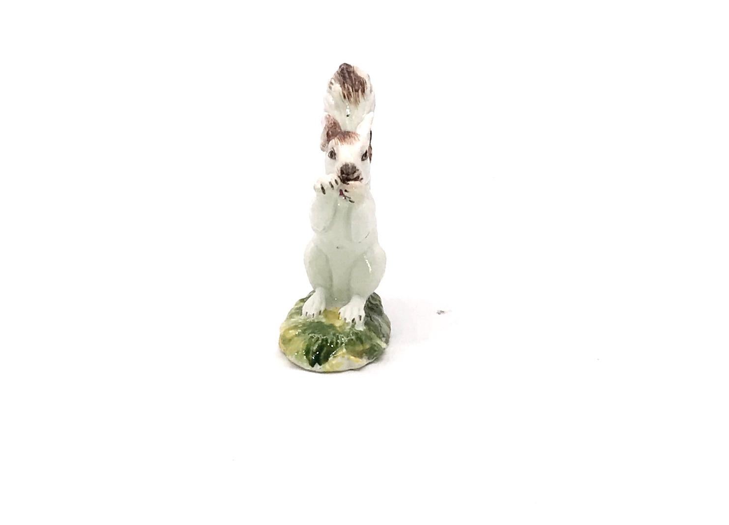 Rare Antique white squirrel with brown accents, clasping a nut between its paws and perched on a green base, 2.5 high by 1.5 inches wide, made by the Derby factory in the eighteenth century. This is the smaller of 2 different sizes of squirrels
