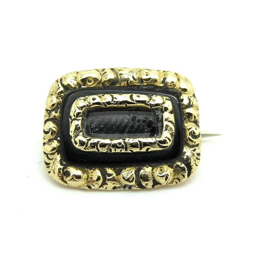 Questa squisita spilla antica da lutto vittoriana è finemente realizzata in oro 9ct, con intricati dettagli incisi e ricco smalto nero che circonda un pannello centrale di capelli intrecciati. La combinazione di materiali riflette la natura