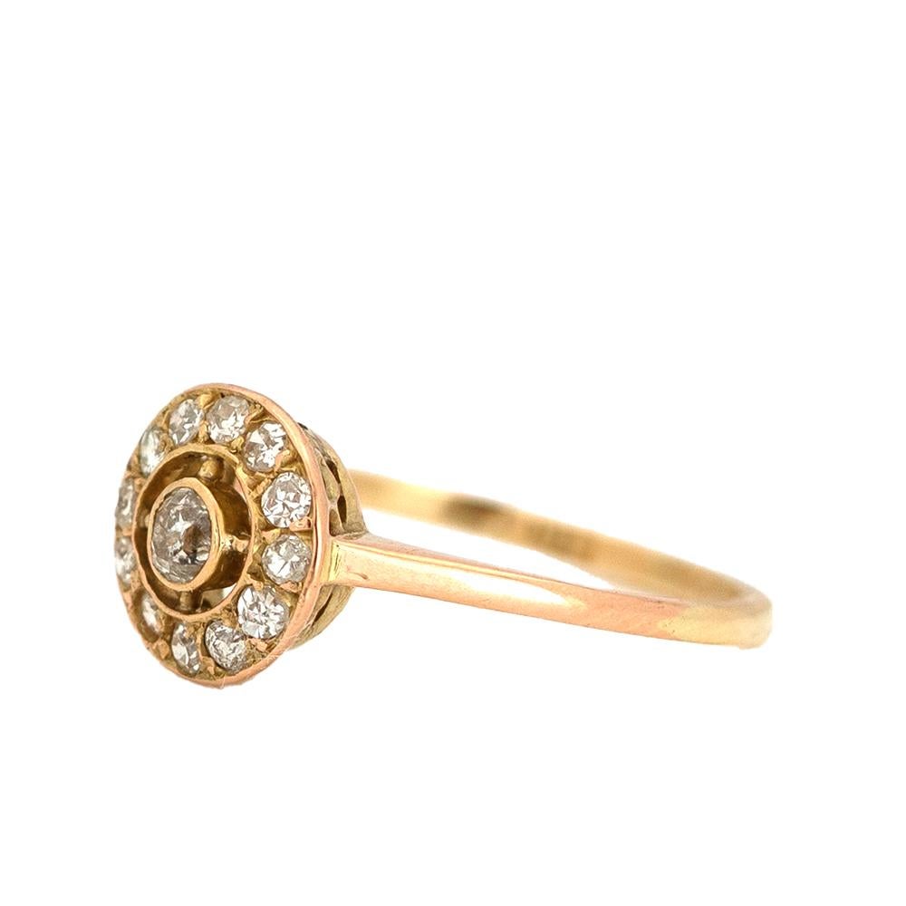 Cette bague ancienne raffinée date du début des années 1920 et présente une monture classique de style cible, avec un diamant central de taille ancienne entouré d'un halo de pierres assorties. Le Design-Light crée une élégante symétrie, adoucie par