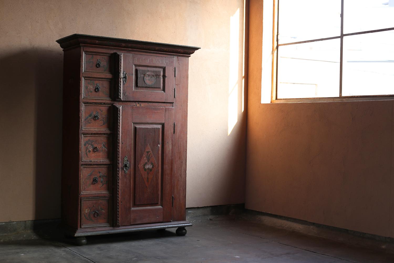 Antiker italienischer Schrank.

Dieser bemalte Schrank aus dem Jahr 1835 wurde vermutlich in der Region Trentino-Südtirol in den norditalienischen Alpen hergestellt.

Die aus robustem Kiefernholz gefertigten Türen und Schubladenfronten sind mit