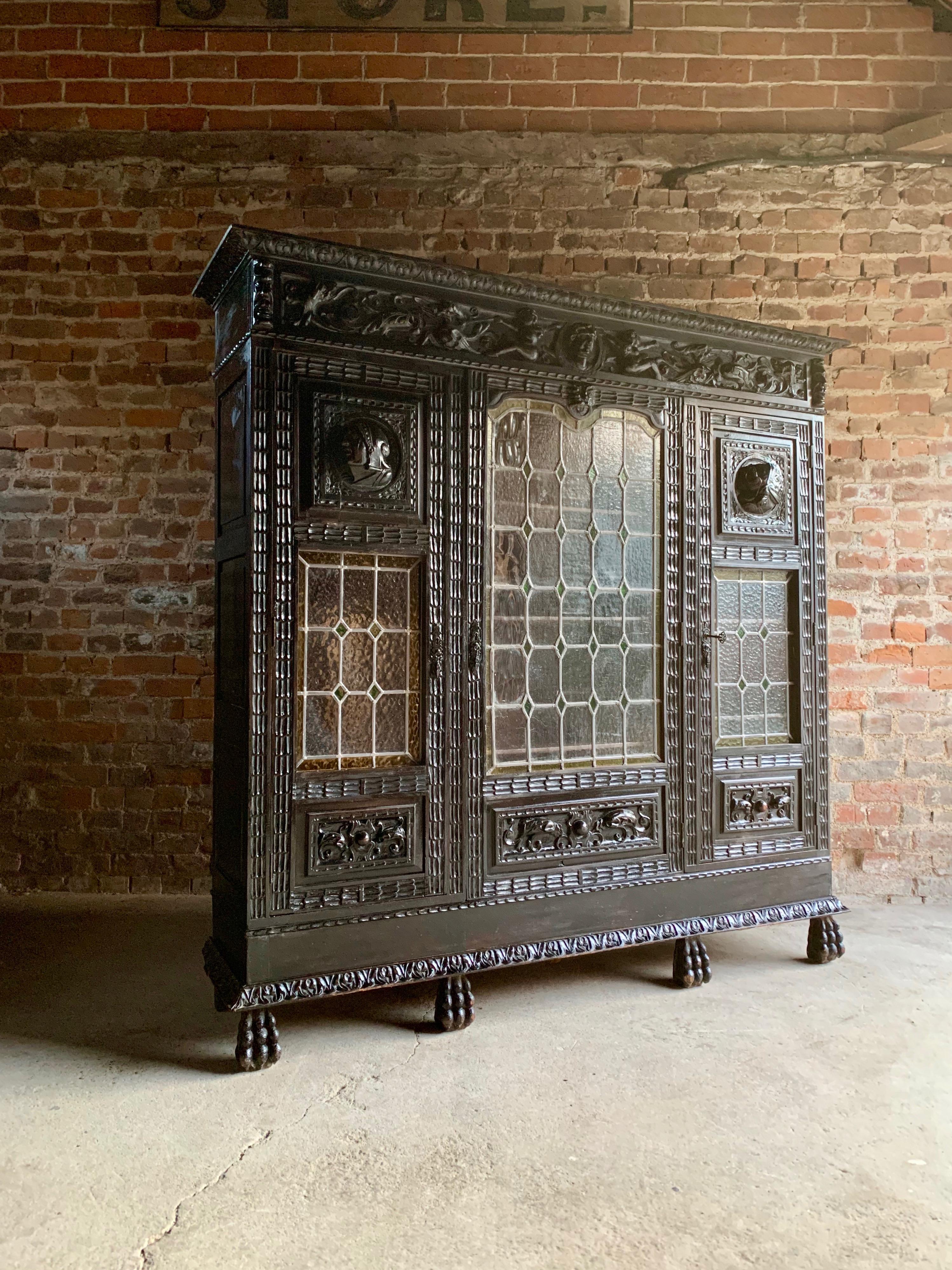A magnificent 19th century Victorian era heavily carved and Ebonized oak north European cabinet / bookcase circa 1880, the corniced top over three leaded glazed doors each with three shelves within, carved figural, floral and mask decoration all