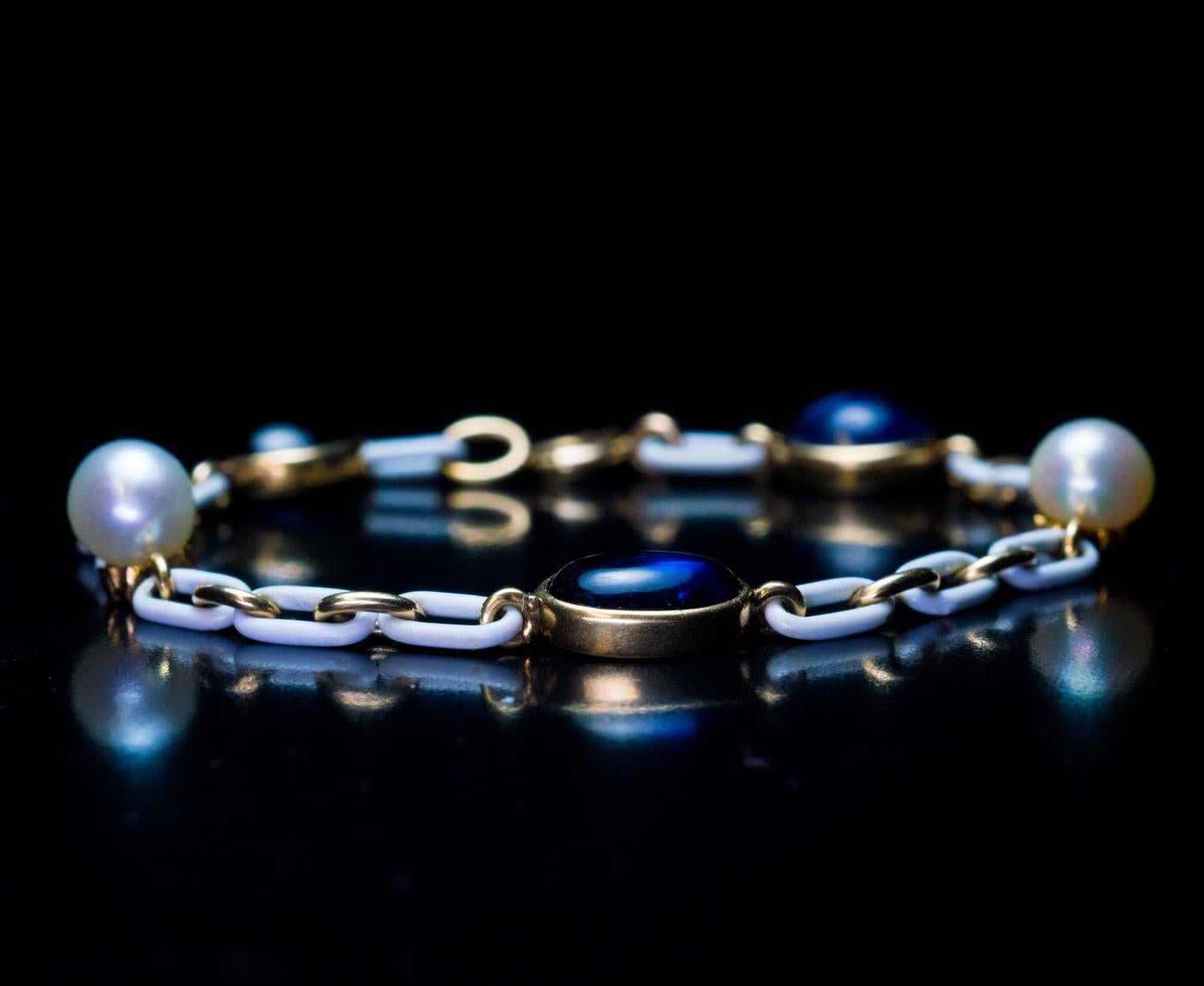 Circa 1910

This stylish and unusual Edwardian era antique bracelet is crafted in 14K gold. The wider links of the bracelet are covered with opaque white enamel. The bracelet is embellished with two pearls (6 mm each) and three cabochon cut natural