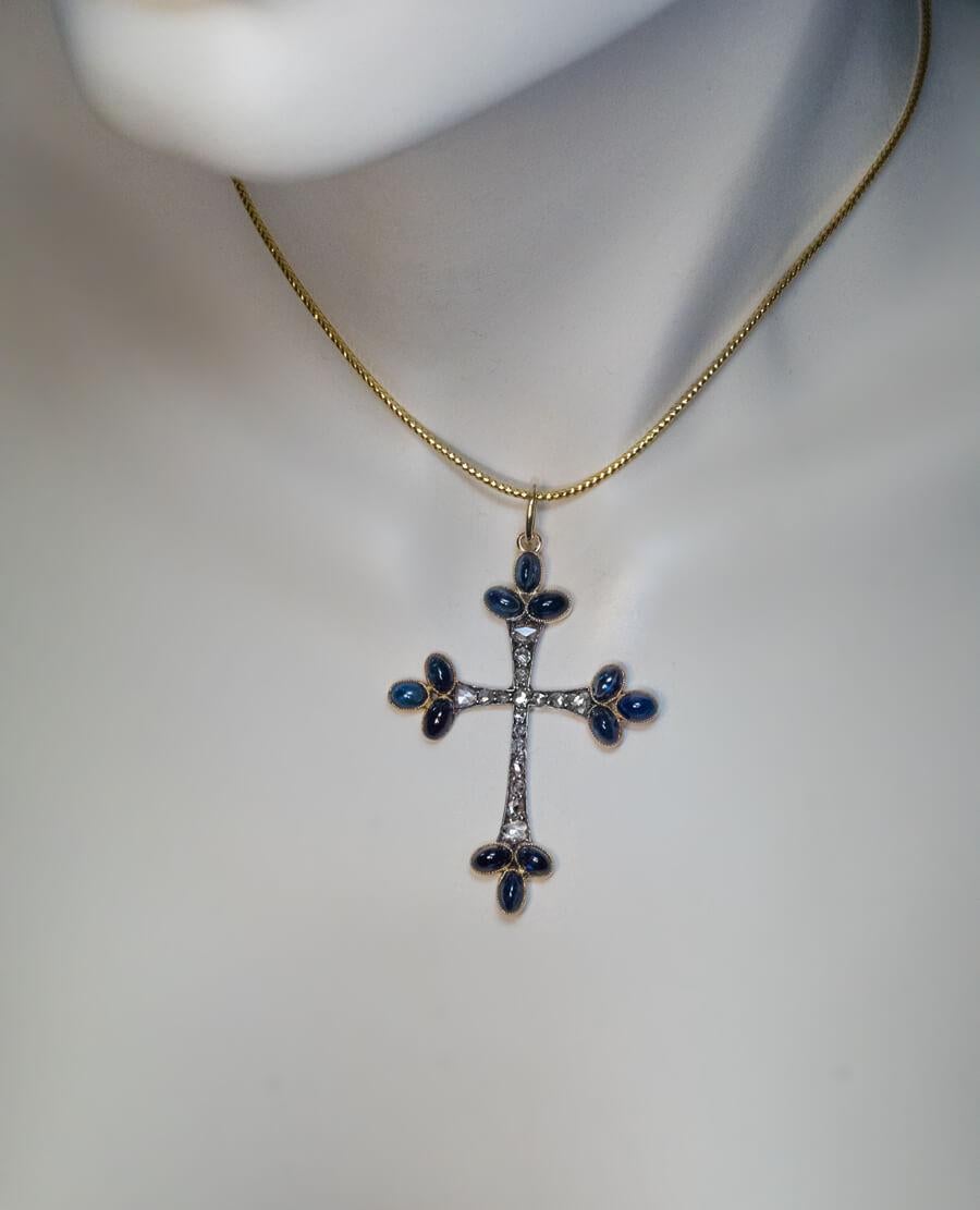 Circa 1890s
The cross pendant is finely crafted in 14K gold and silver. It is embellished with cabochon cut blue sapphires and old rose cut diamonds.
The design of the cross is influenced by the Art Nouveau style of the period.
The cross measures