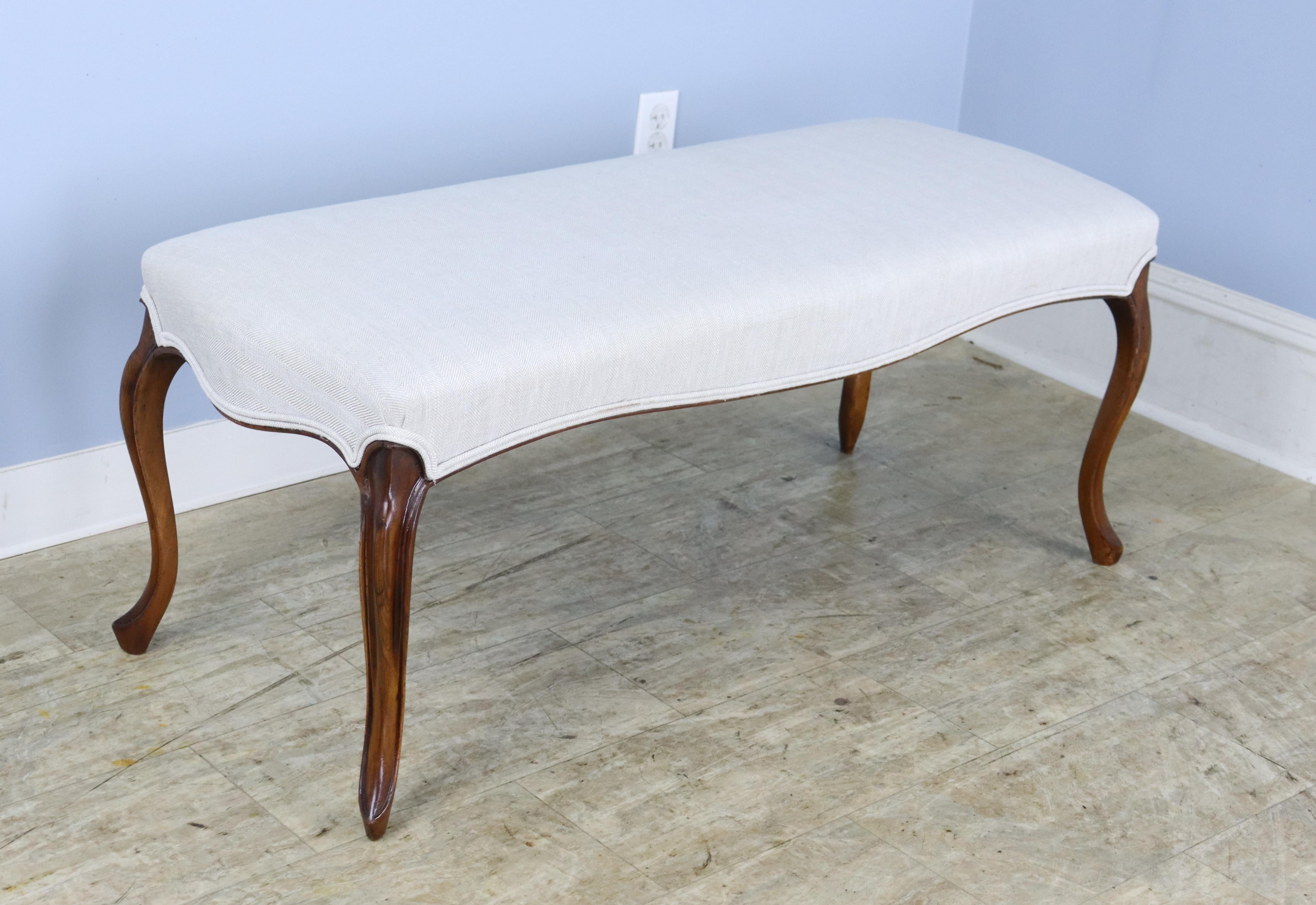 An elegant cabriole leg bench, newly upholstered in cream linen with double piping at the edges.  Glossy curved mahogany legs with good color and patina. 