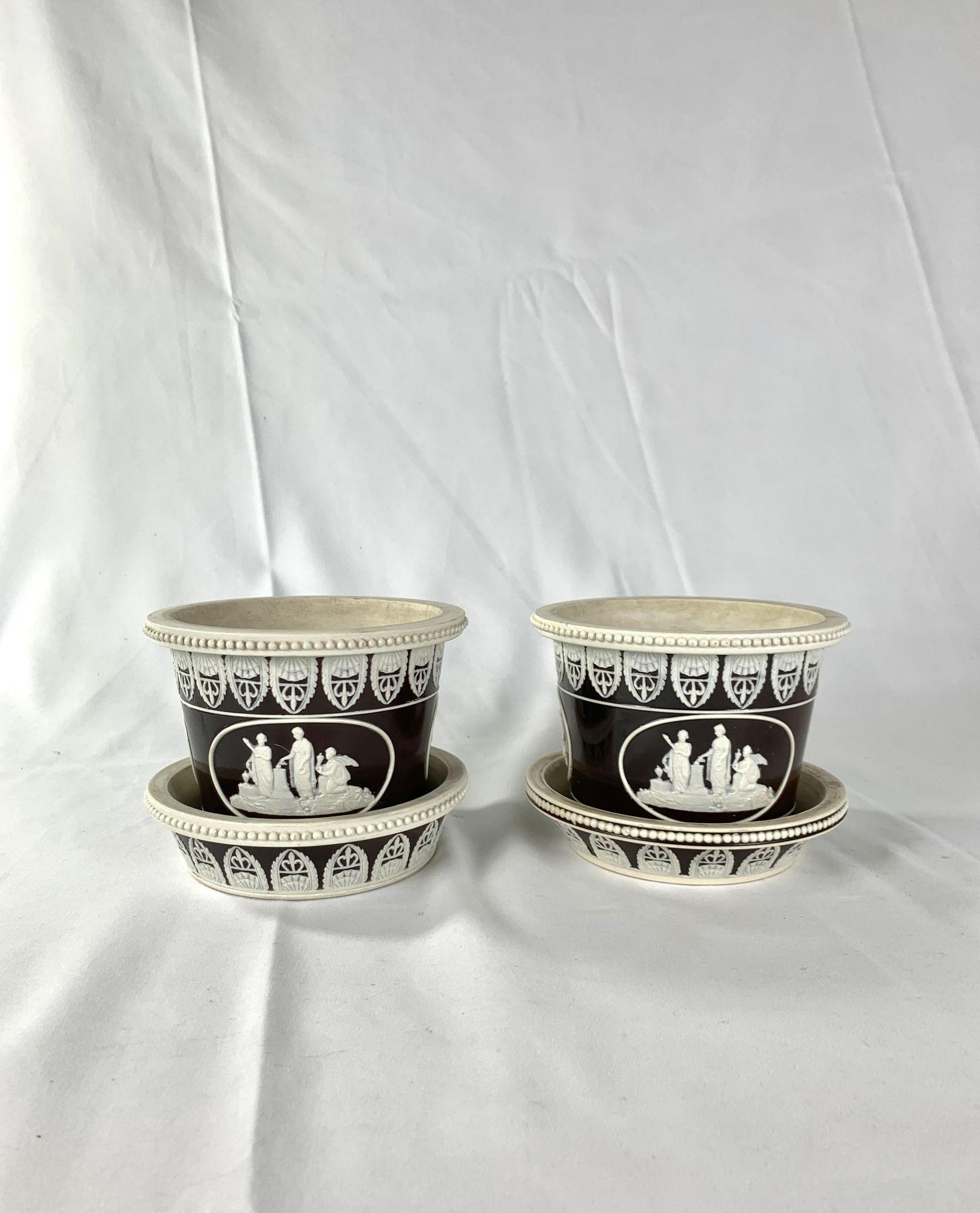 A pair of lovely Ridgeway stoneware cachepots and stands with neoclassical decoration and three scenes in cartouche.
The design is done in white relief on dark ground and is crisply modeled.
The central scene portrays a classical offering to the