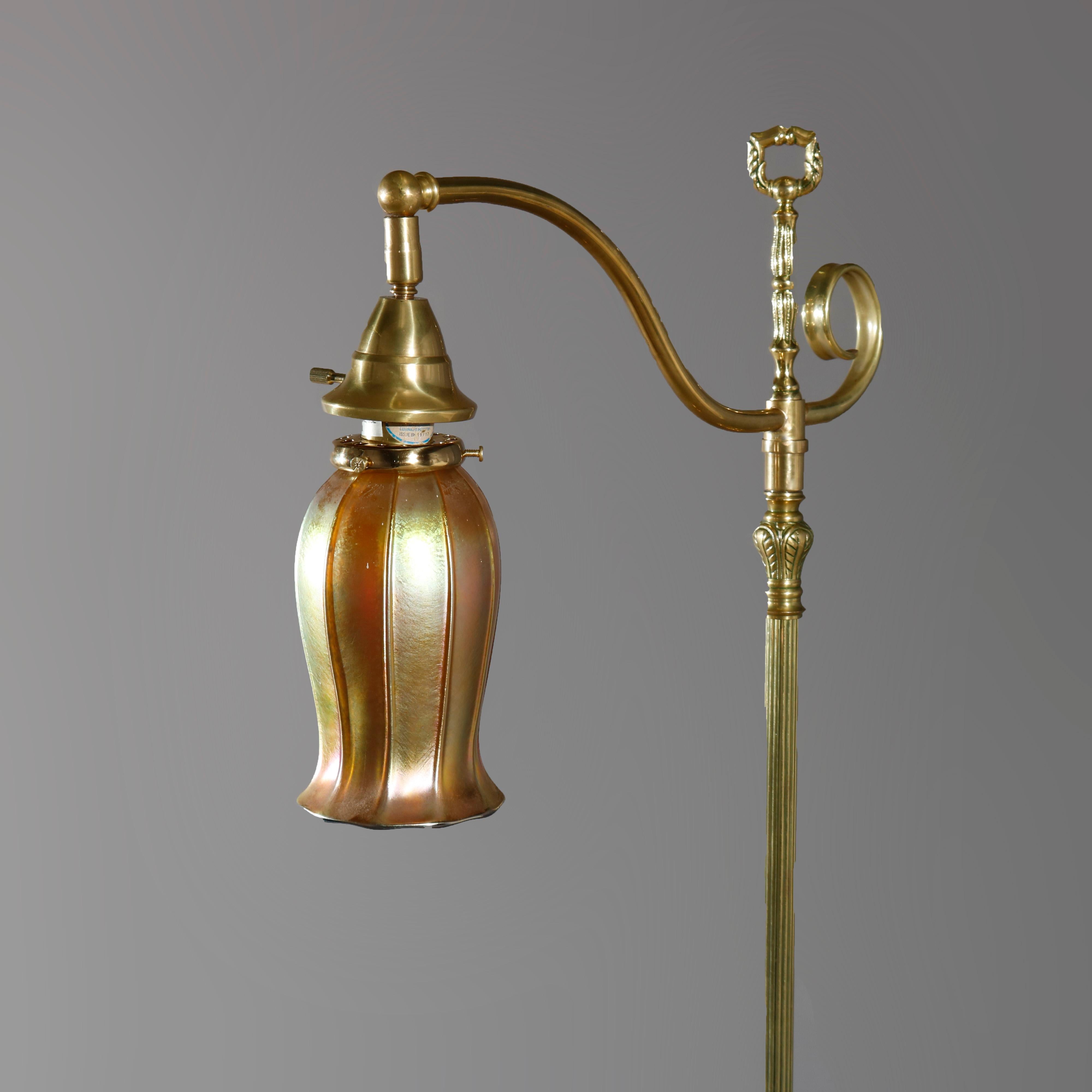 An antique Arts and Crafts floor lamp in the manner of Caldwell offers brass construction with reeded post having central pierced element, scroll form arm terminating in gold aurene Steuben art glass shade, and raised on square base having stylized