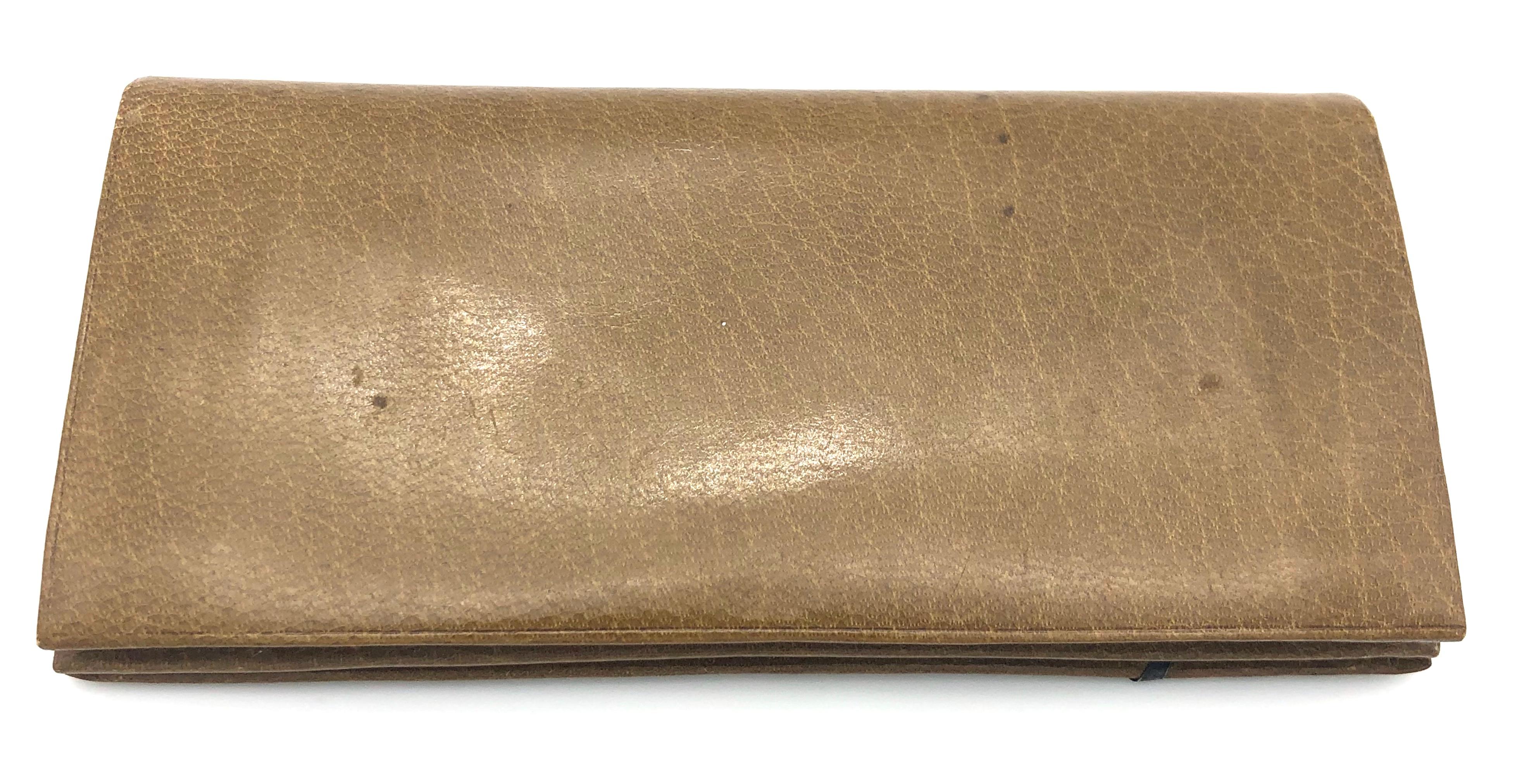 Antique beige calf leather foldable flap wallet in a landscape format decorated with a silver holly berry leave. It has a coin pouch with a clasp closure, as well as bill compartments. It is embossed 