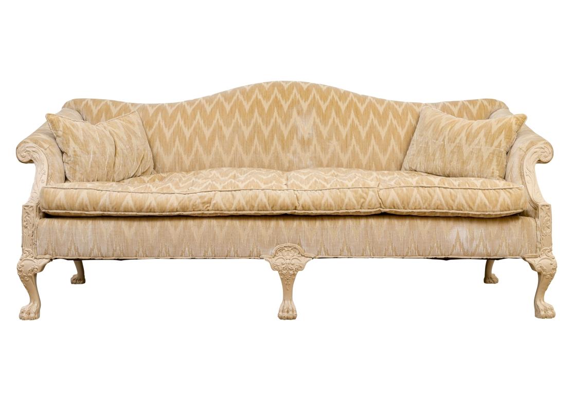 Antique camelback sofa with strongly carved frame and legs in a paint decorated finish.
The sofa with a long button tufted seat cushion secured with elastic bands along with two matching down filled zippered accent pillows. Upholstered in a soft