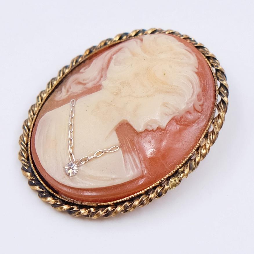 This delicate cameo pendant-brooch depicts a portrait of a young lady interestingly decorated with a rhinestone. Can be worn as a brooch or attach a chain to the bail and wear it as a pendant.
Materials: Base metal, plastic, rhinestone
Height: 1.77