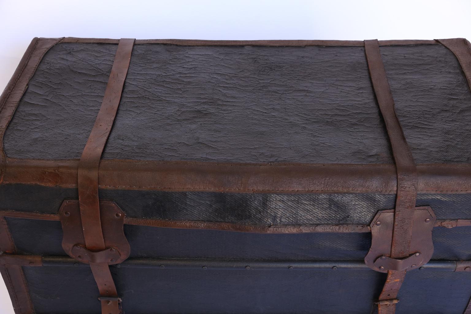 Antique travel trunk found in France. The trunk is covered in waterproofed canvas with sturdy wooden braces on the bottom. The exterior features restored leather corner caps, heavy leather straps secure the lid with brass buckles, wide leather