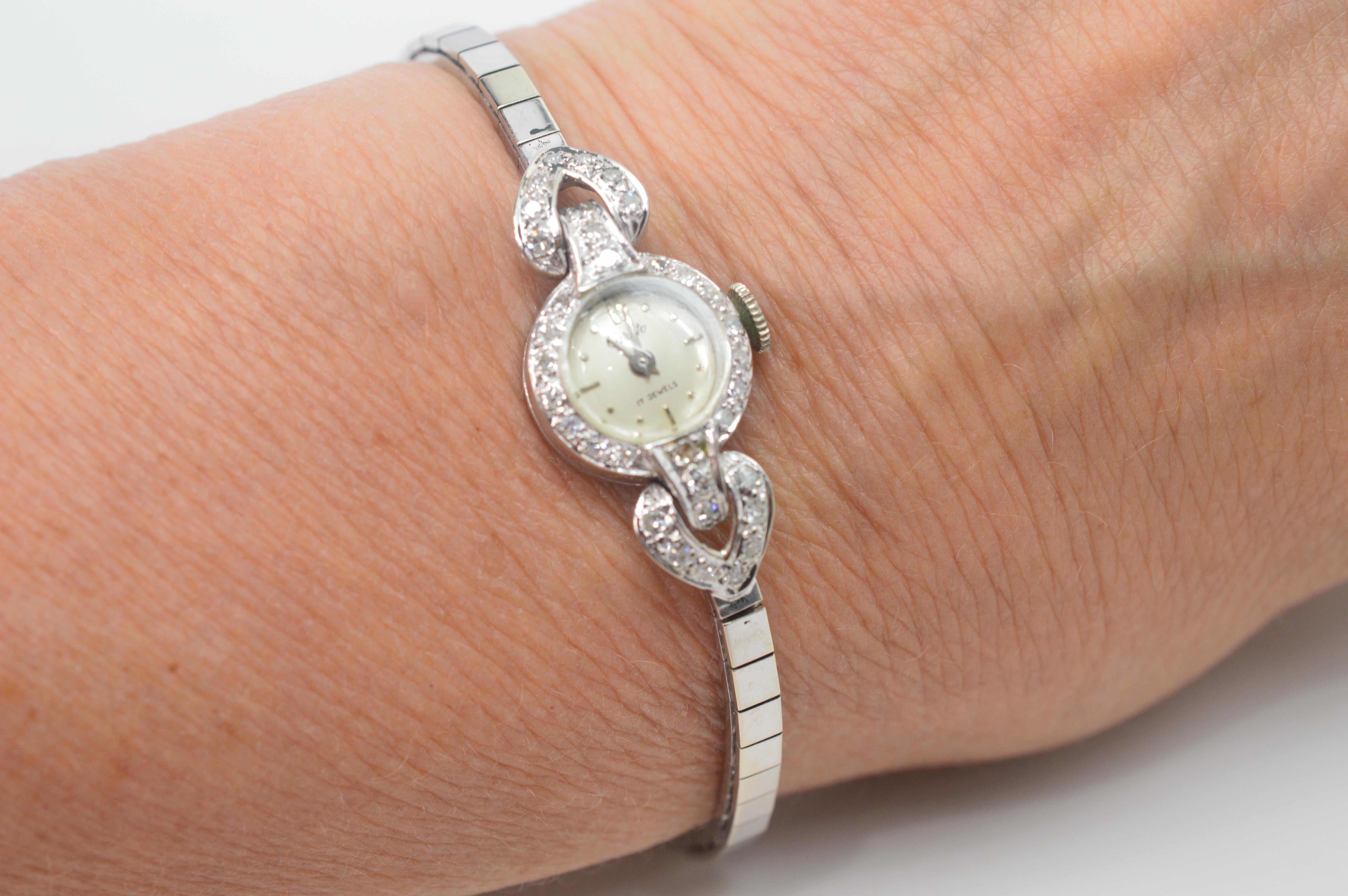 Fine and feminine in 14 karat white gold, this women's antique dress watch by Carlto is exquisite.  Thirty six H/I1 diamonds, totaling .30 carat TW adorned it's petite 1/2 inch round case and heart-shaped side hinges. The attractive slender bracelet