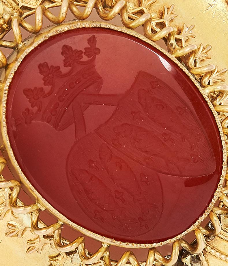 

Shield design, set with oval carnelian, carved in detail with two coats of arms below a coronet, 5.7cm, 18.2g.