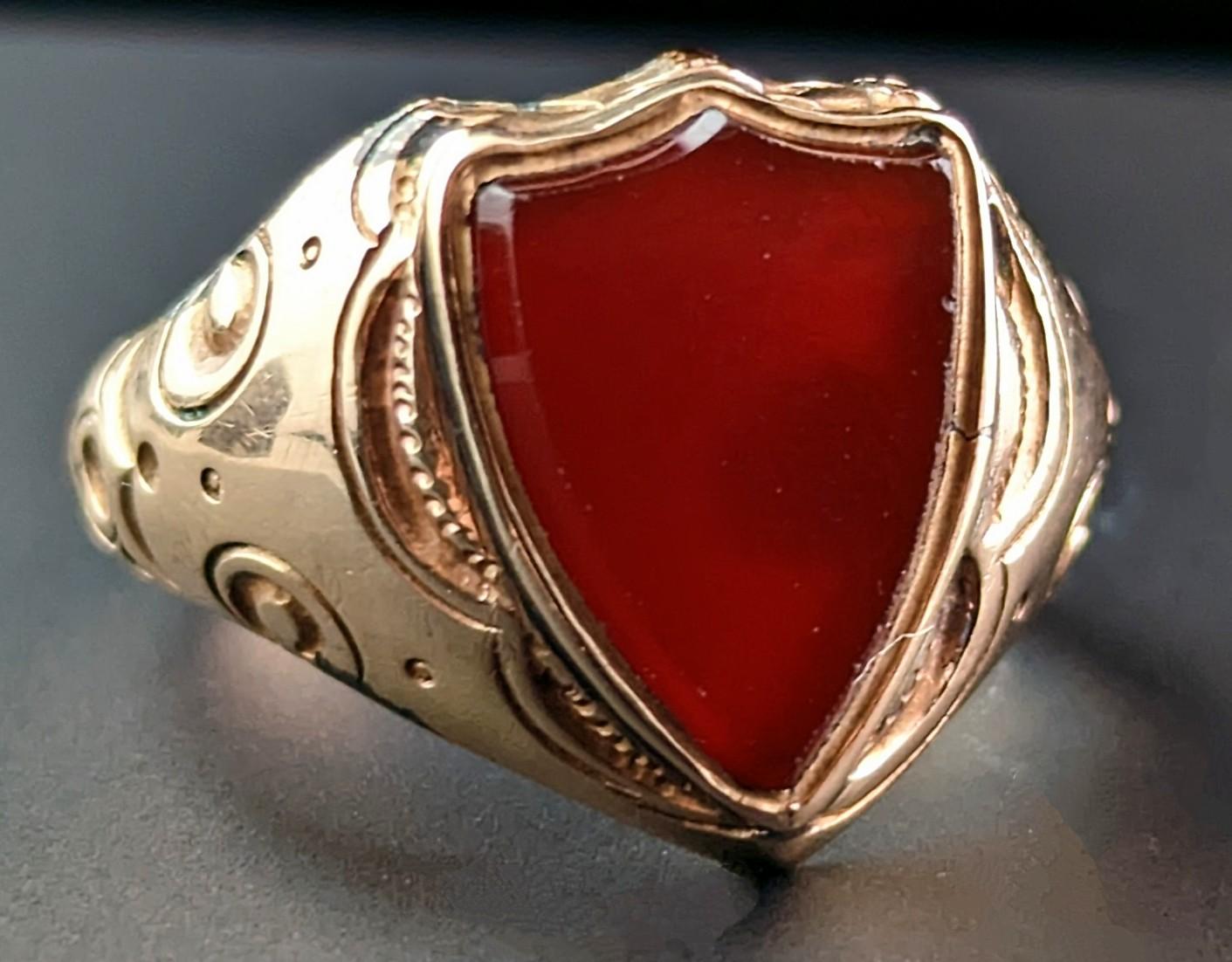 This antique, Edwardian era 9kt gold and Carnelian signet ring really has a lot going on!

It is truly a statement signet ring and is very grand and regal with an unusual design.

It has an shield shaped face set with a rich orangey red Carnelian