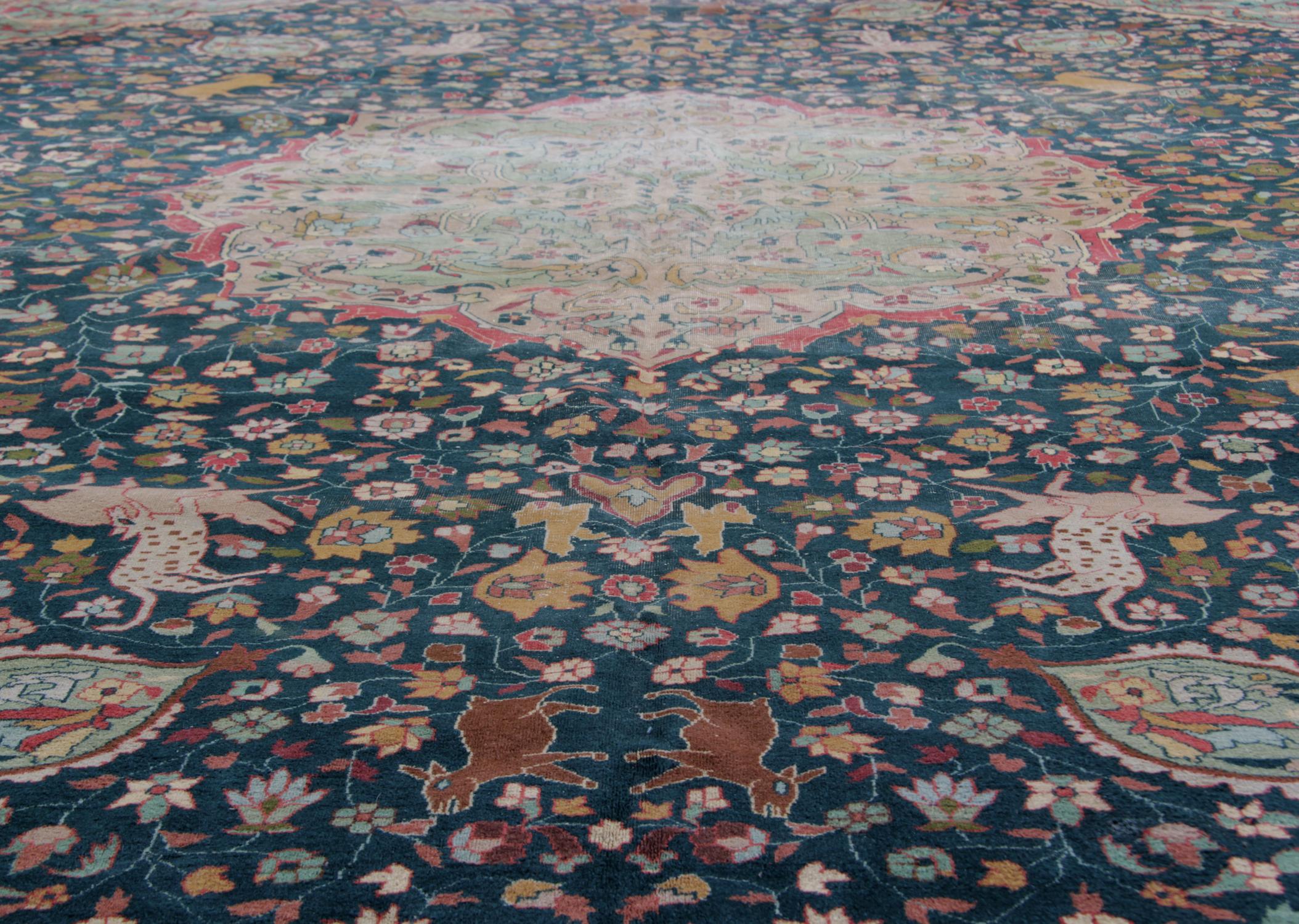 This large handmade indian rug features intricately woven animal and floral motifs, woven in a circular design on a dark background around the contrasting light green central motif. Handspun wool and cotton have been used in the construction of this