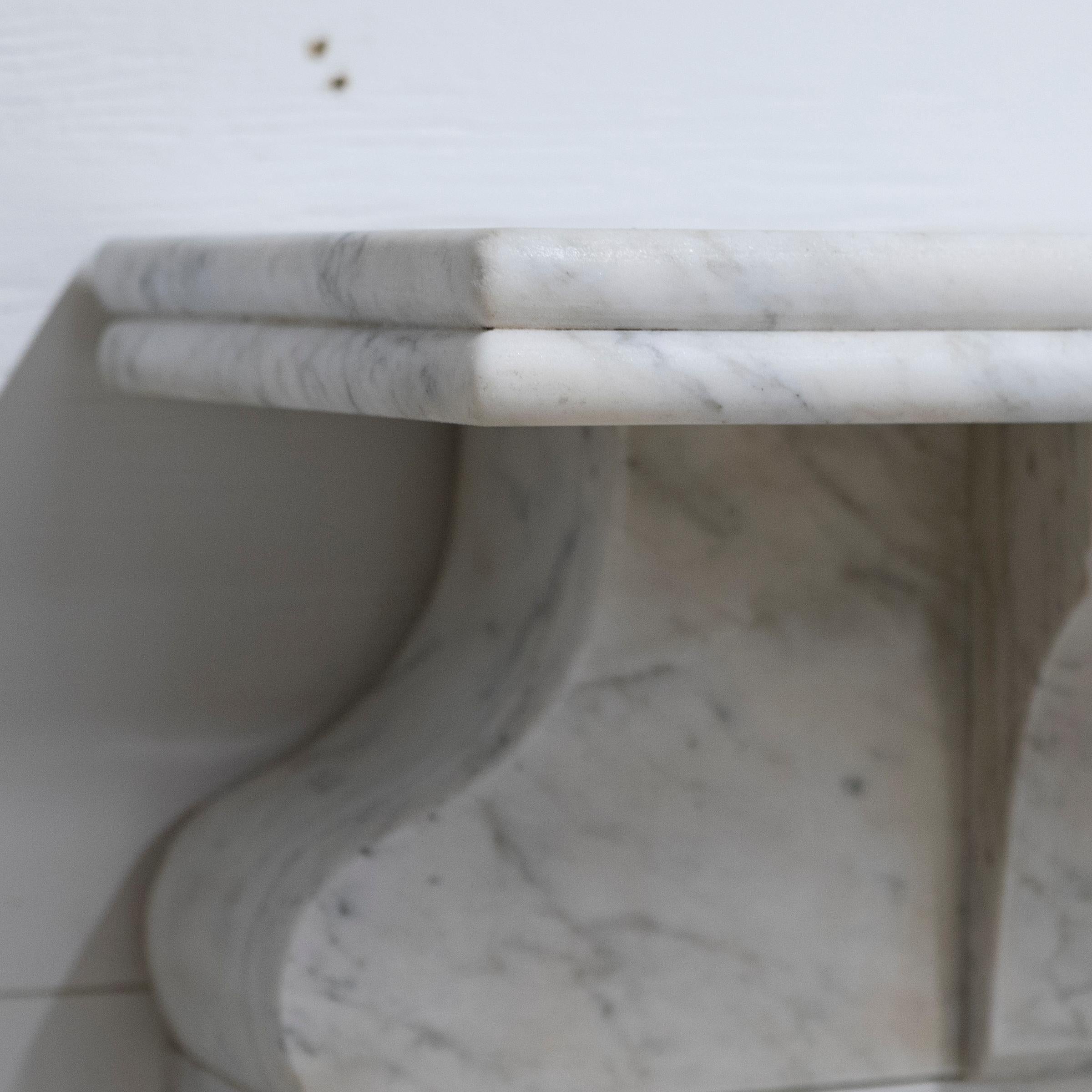 Of rare design and generous height, this chimneypiece is carved from fine Carrara marble. 

The lintel is comprised of two elements; the higher component has 3 simple corbel forms to support the bevelled mantle shelf. Thumbnail details are seen