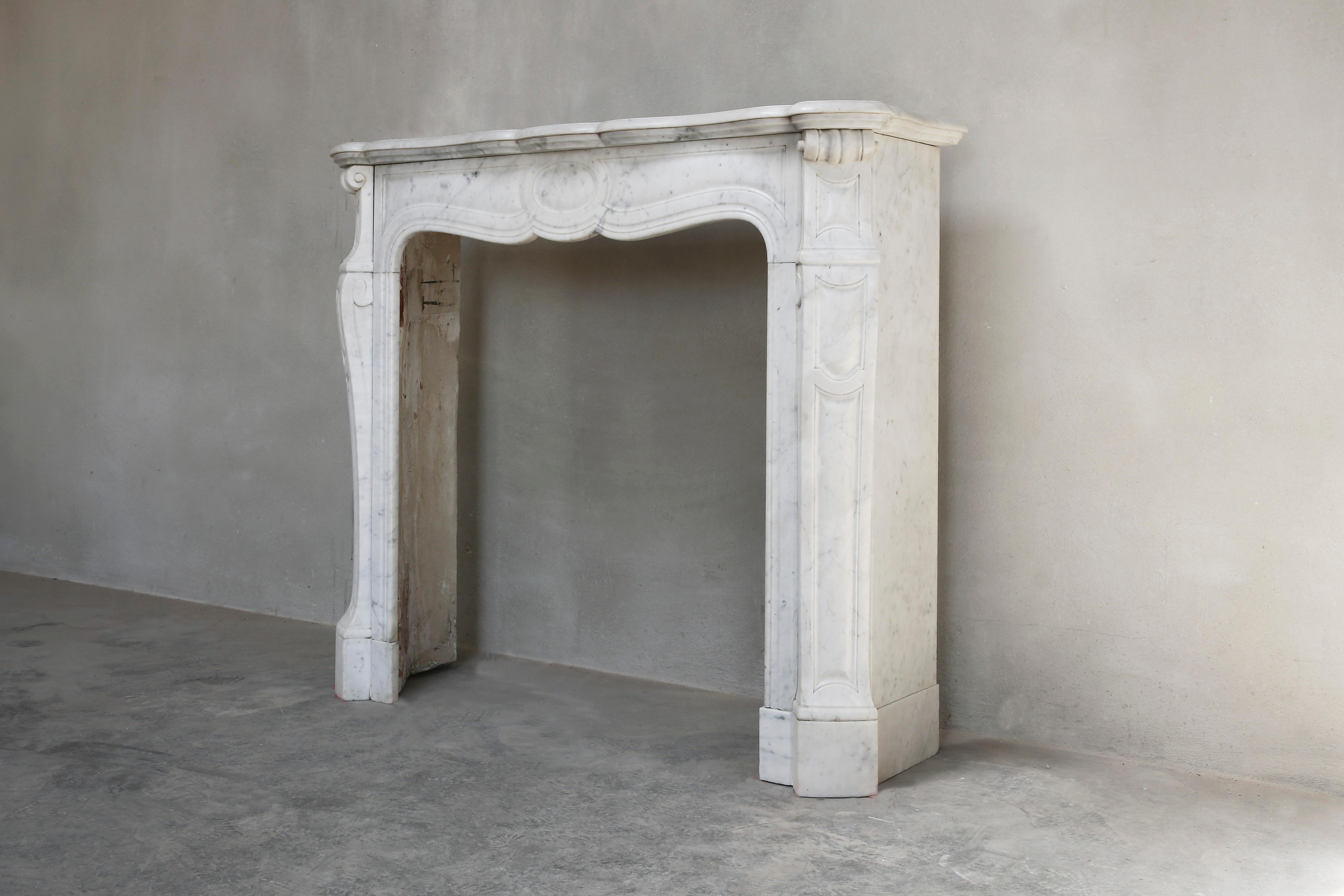 Beautiful Pompadour fireplace from the 20th Century. Pompadour fireplaces are generally slightly smaller in size and are very elegant due to the round shape and ornament in the middle. The marble type of this fireplace is Carrara marble. This type