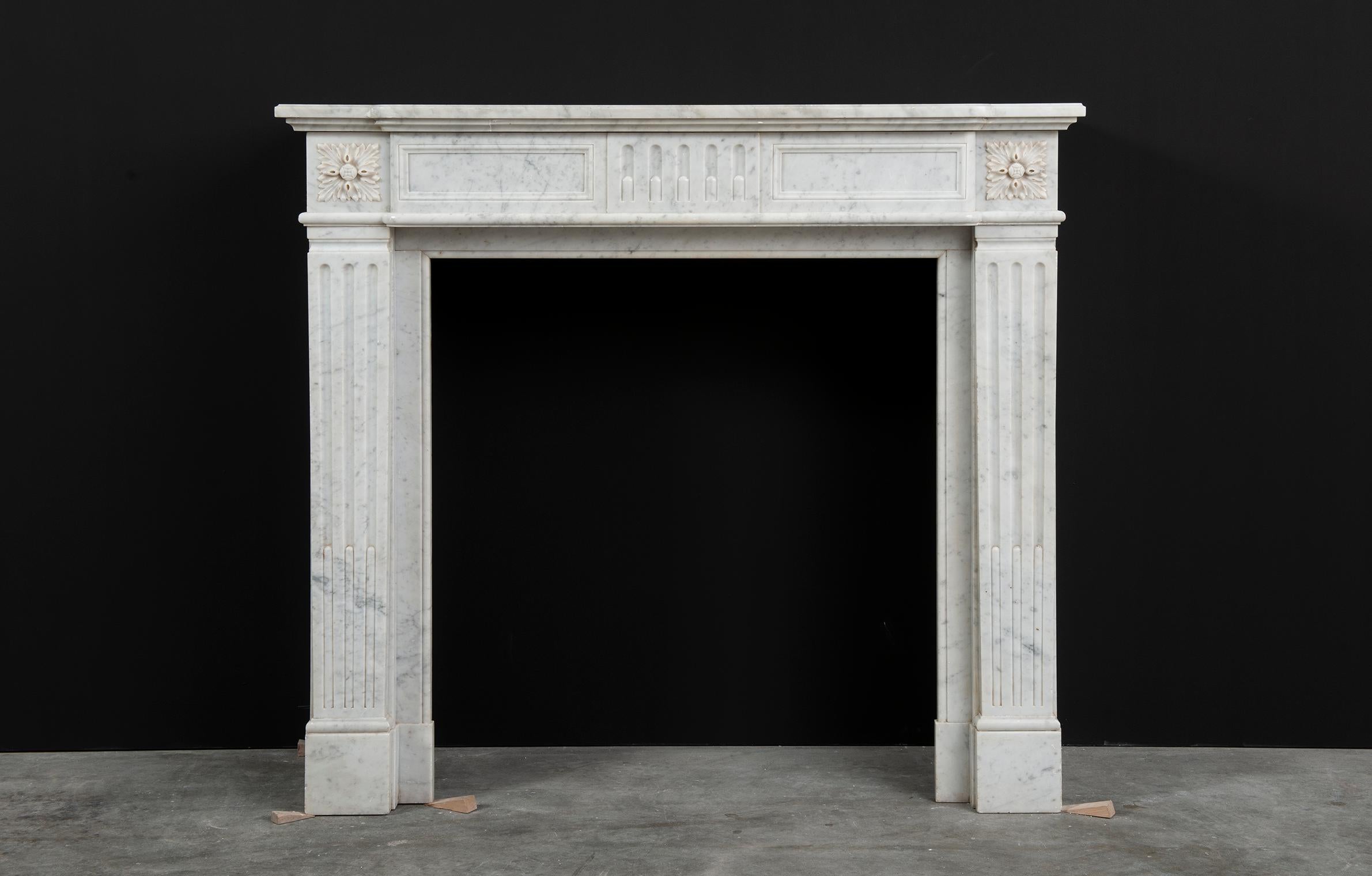 Happy to offer this small and lovely Louis XVI fireplace mantel in Carrara white marble. 

The moulded breakfront shelf sits above a paneled frieze centred by flutes adorned by acanthus paterae endblocks on both sides. These enblocks rest on