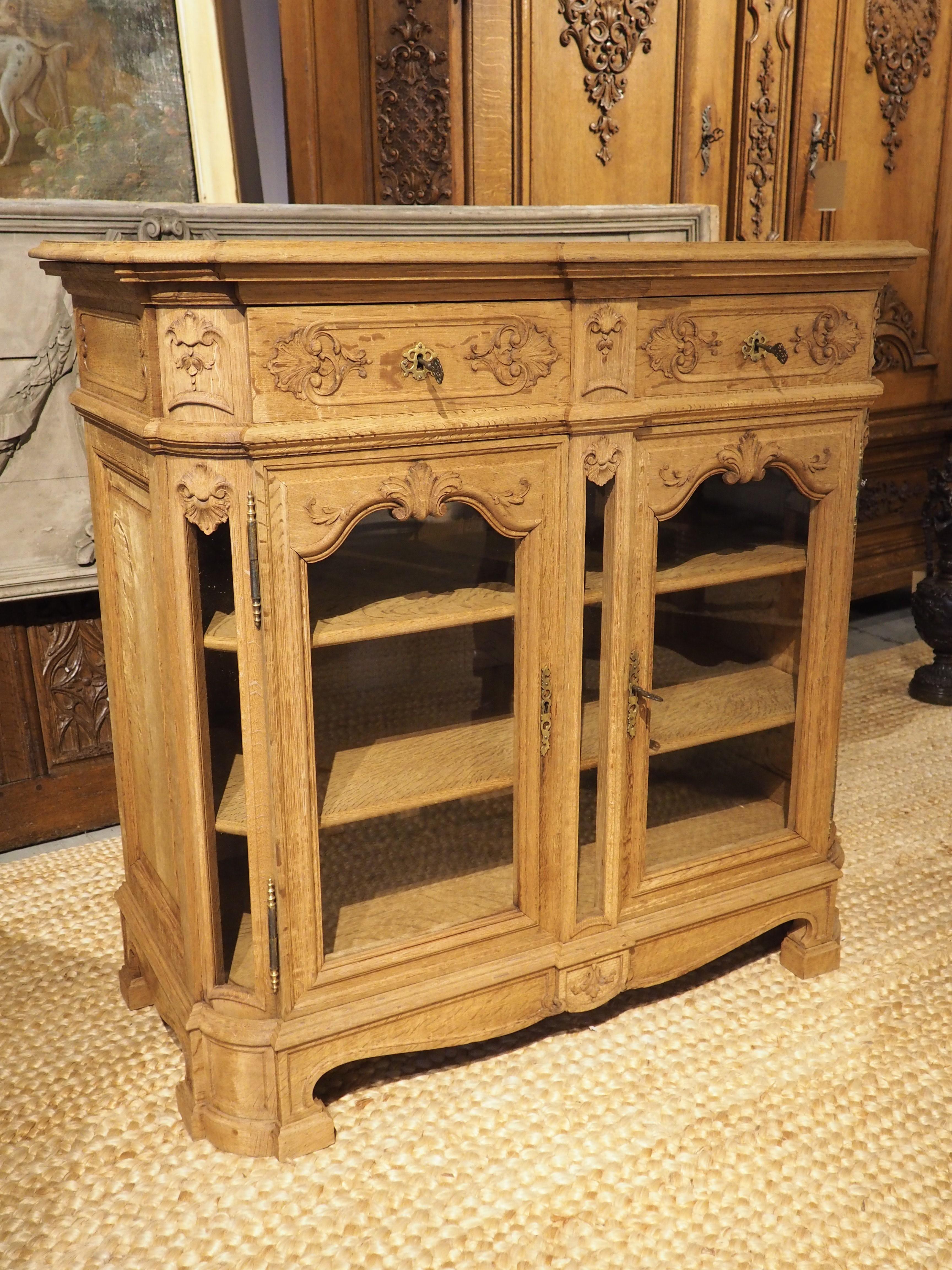 Featuring elements in the style of both Louis XIV and Louis XV, this buffet vitrine is from Liege, Belgium. Hand-carved circa 1900, the wood has been bleached more recently, giving the vitrine a light oak honey color with fascinating visible