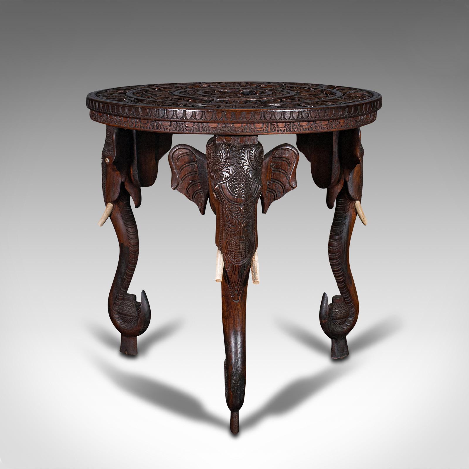 This is an antique carved circular table. An Indian, teak colonial campaign table with elephant masques, dating to the late Victorian period, circa 1900.

Enthusiastically carved table with charming legs
Displays a desirable aged patina