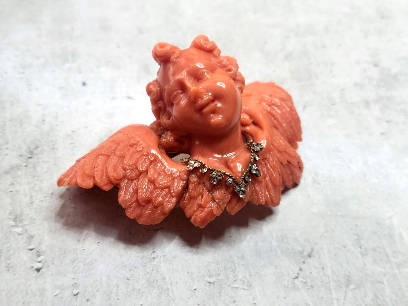 We present a true work of art to your attention - a rare and unique brooch carved from a single Italian Mediterranean coral Sciacca. This antique brooch, made in the form of a putto - a little boy angel with a diamond necklace, is imbued with the