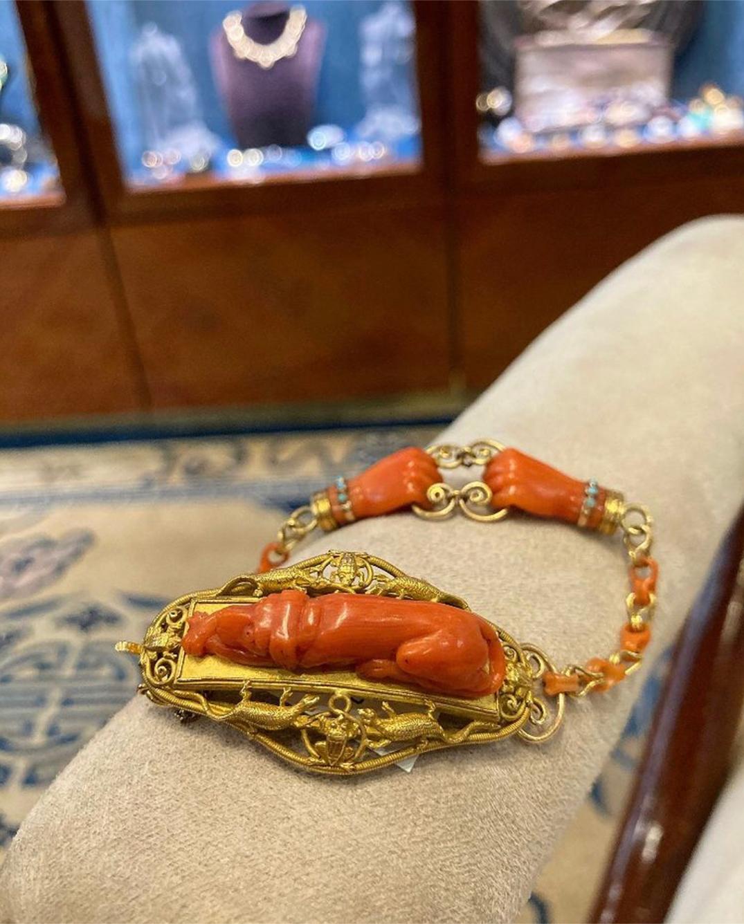 An antique nineteenth century carved coral hunting bracelet with turquoise embellishment, in yellow gold. Features a center panel depicting a hound accompanied by lizards and frogs, and a pair of clasped hands on the underside of the bracelet. Made