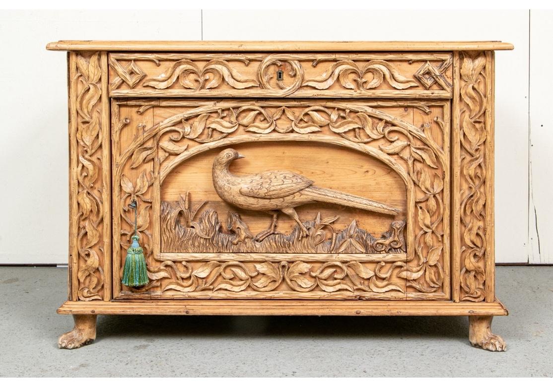 Possibly German. A rectangular cabinet with great overall elaborate carved decoration. The top with plank construction over a frieze drawer. The lower cabinet with a door opening to storage (with a key). Overall carved and applied leafy scrolled